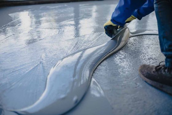 Person in blue jacket and gloves applying gray epoxy flooring to a concrete floor.