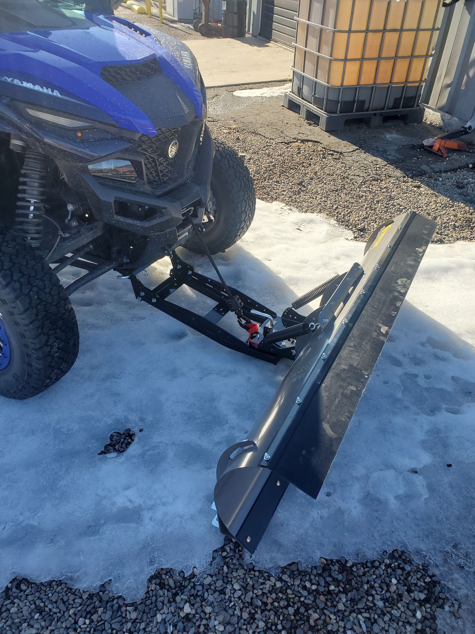 A blue atv with a snow plow attached to it is parked in the snow.