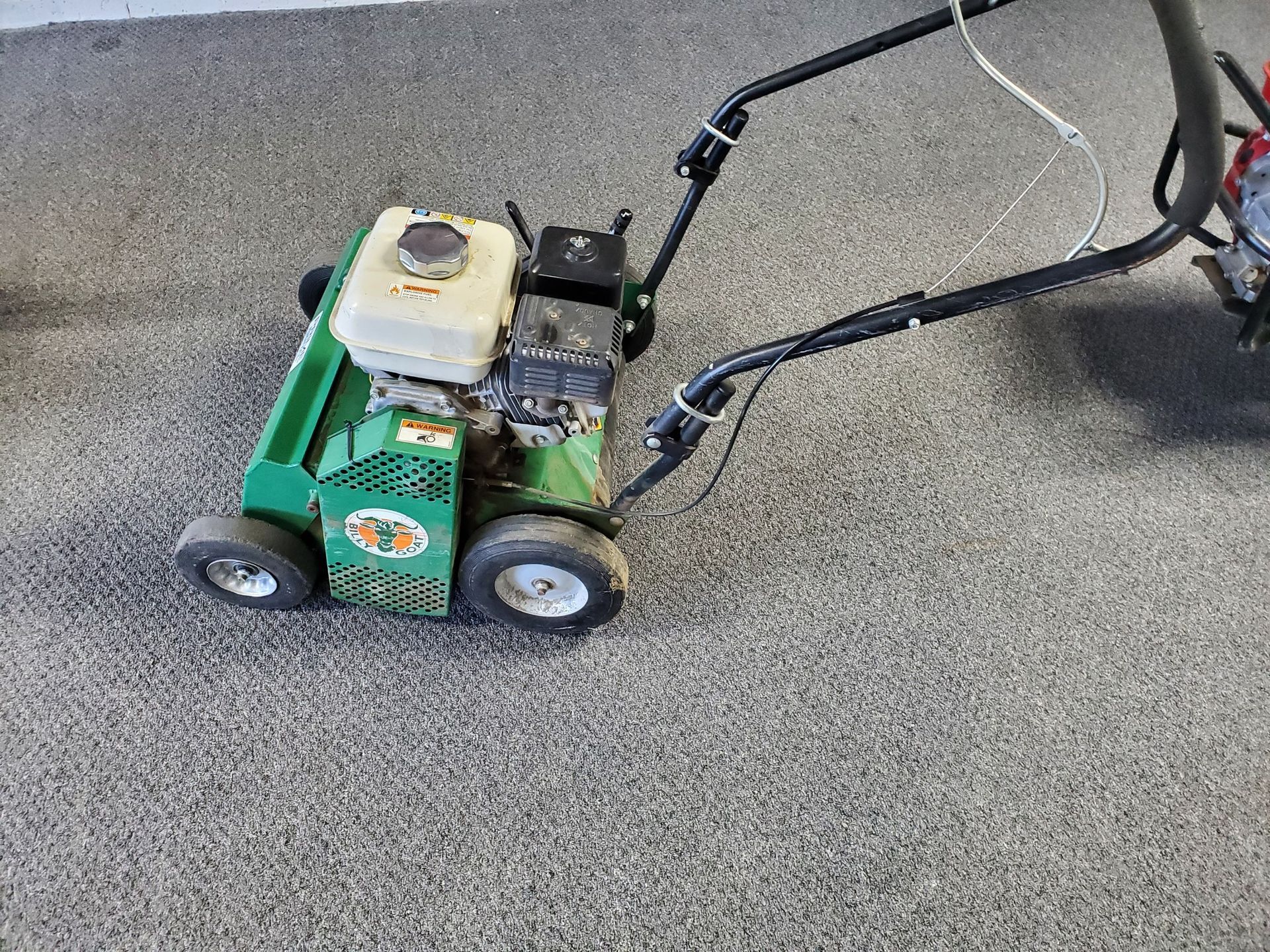 A green lawn mower is sitting on a carpeted floor.