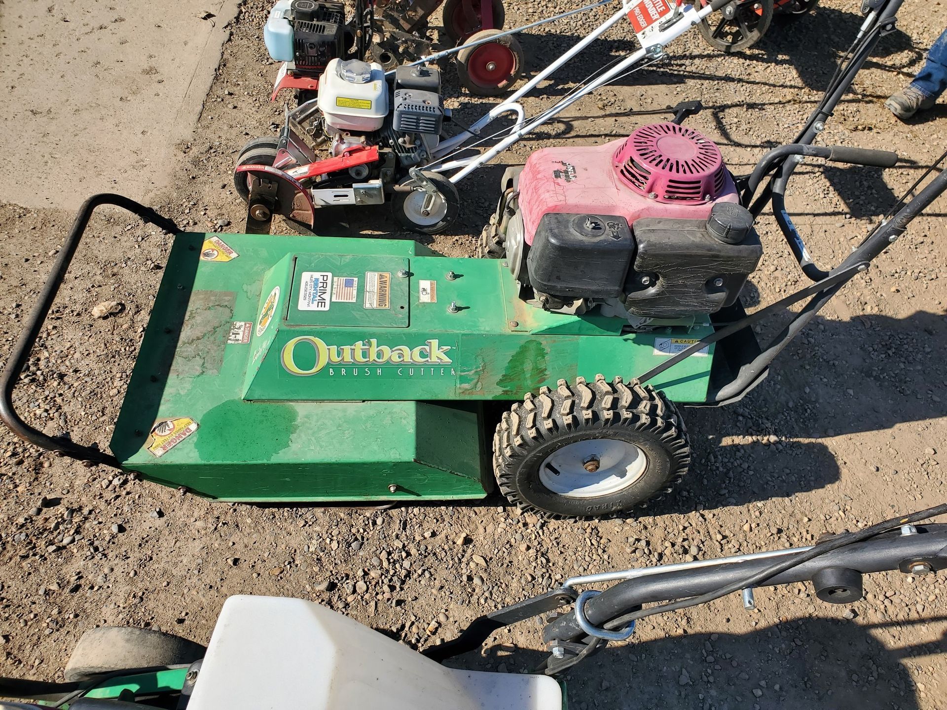 A green outback lawn mower is sitting on top of a dirt field.