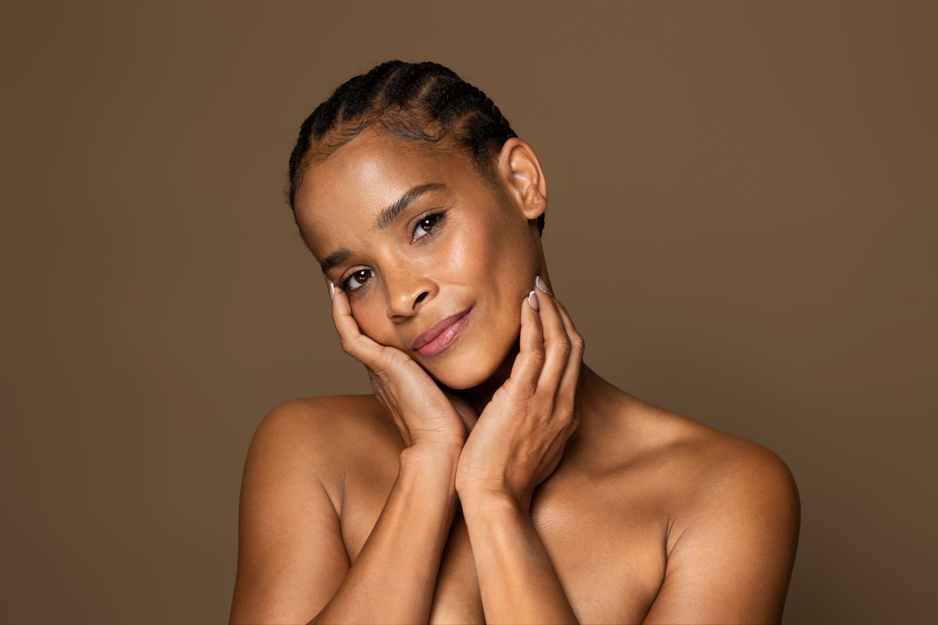 black woman in her 30s with glowing skin touches her face