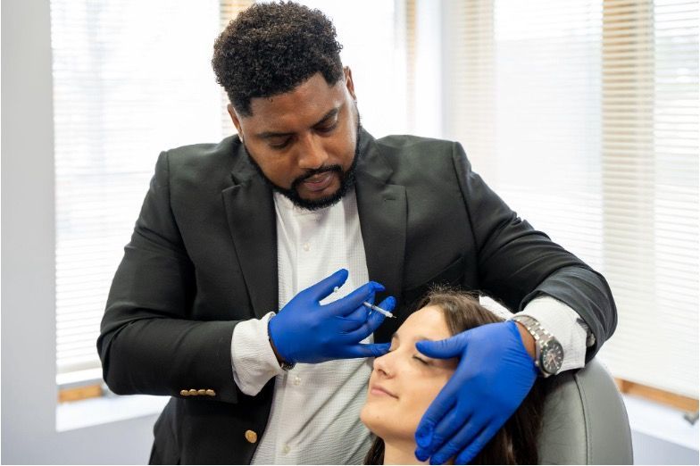 Dentist in black coat and blue gloves examining a patient’s face in a clinic chair