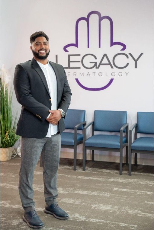 Man standing in a clinic lobby beside Legacy Dermatology sign and blue chairs