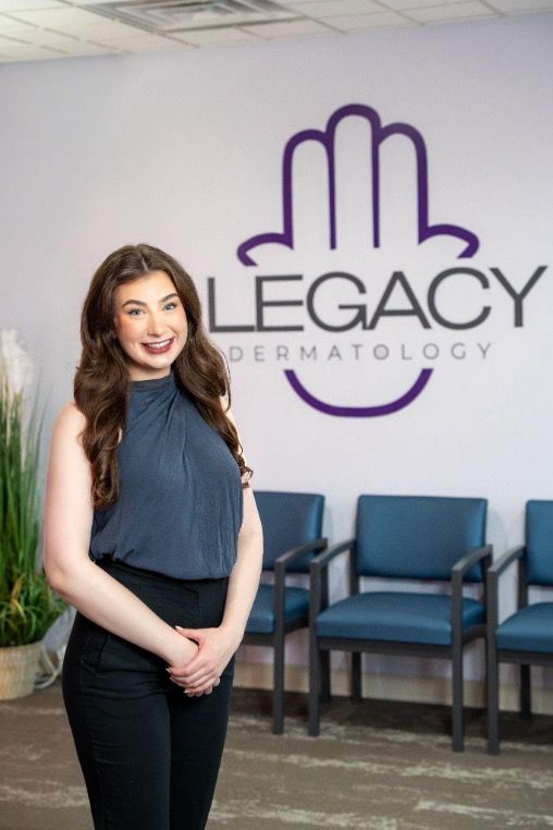 Woman standing in a dermatology office lobby with a Legacy Dermatology sign behind her