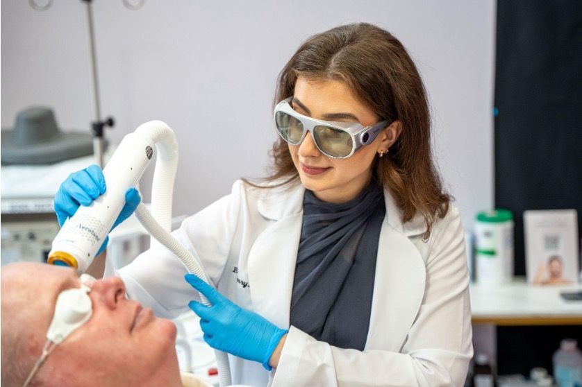 Dentist using a handheld scanner on a patient's mouth, wearing goggles and blue gloves in a clinic.