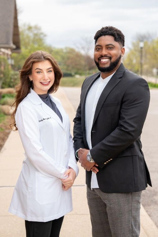 Two healthcare professionals standing outdoors on a sidewalk, smiling at the camera