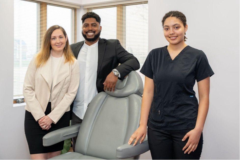 Three staff members standing beside a dental chair in a bright clinic office.