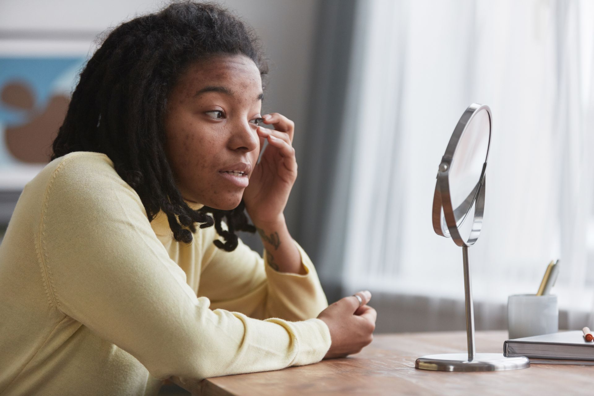 A woman is sitting at a table looking at herself in a mirror.