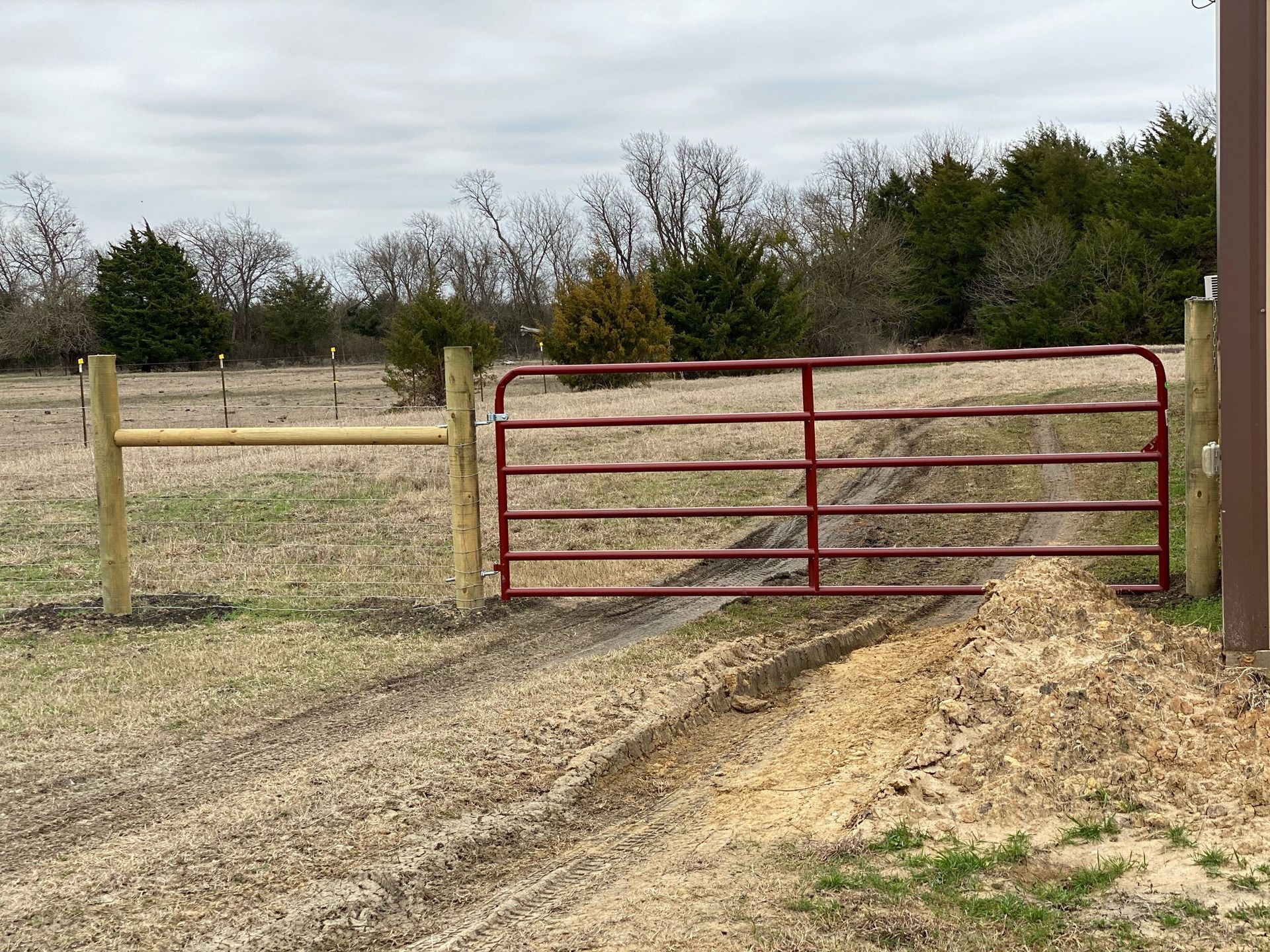 A red gate is sitting next to a wooden fence in a field.