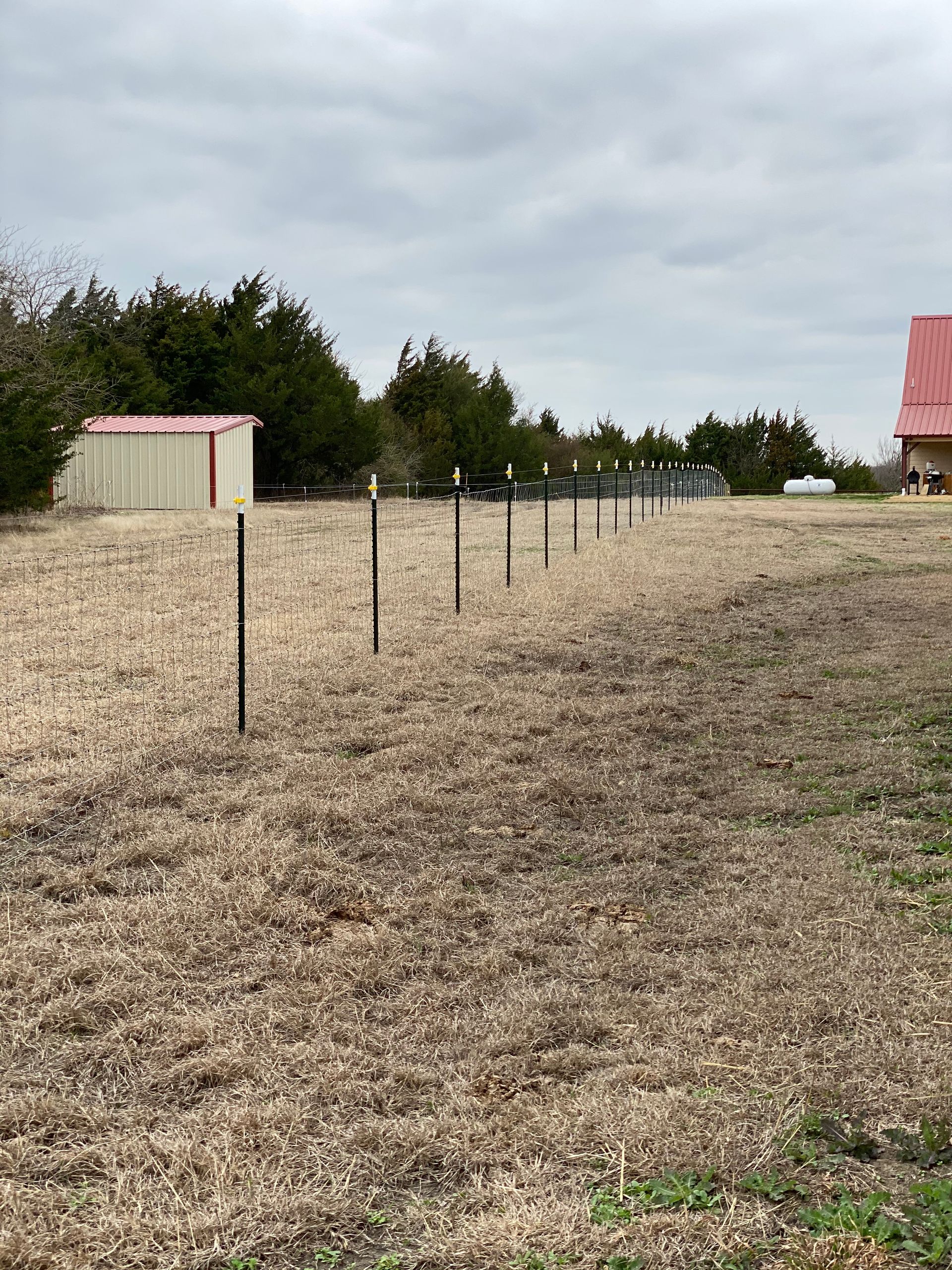A dry field with a red roof and a shed in the background.