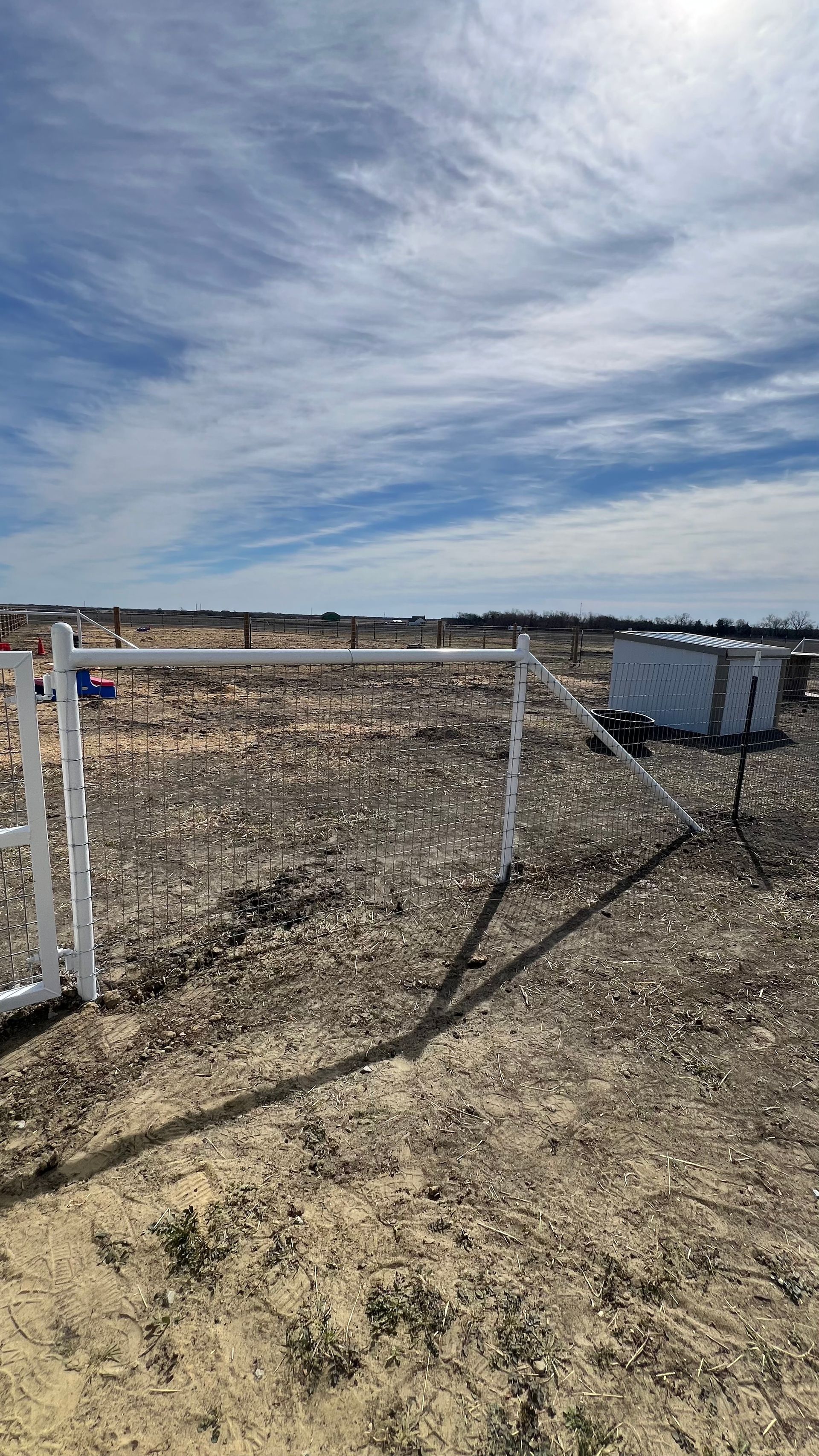 White gate in an open field, with a partly cloudy blue sky.