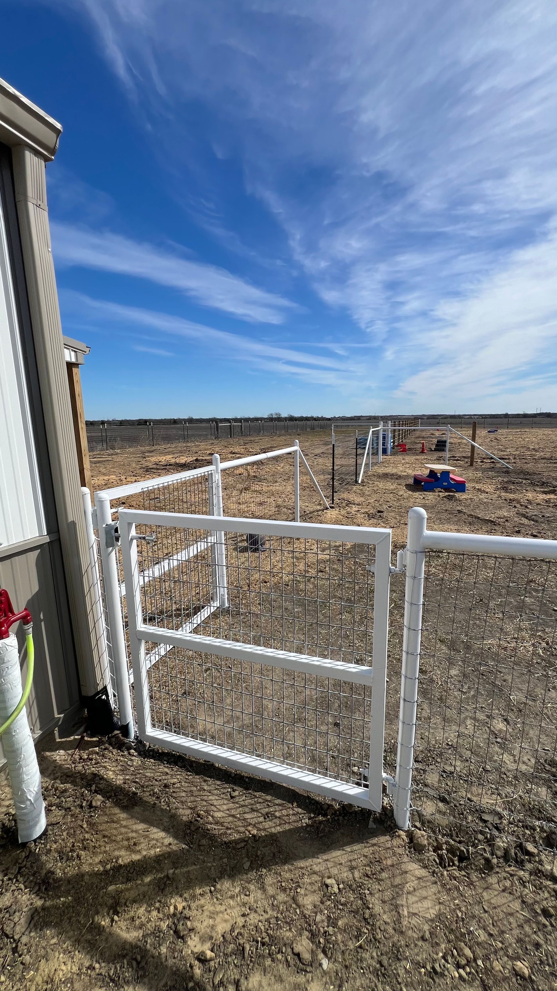 White metal gate and fence in a gravel yard under a blue sky with streaky clouds.