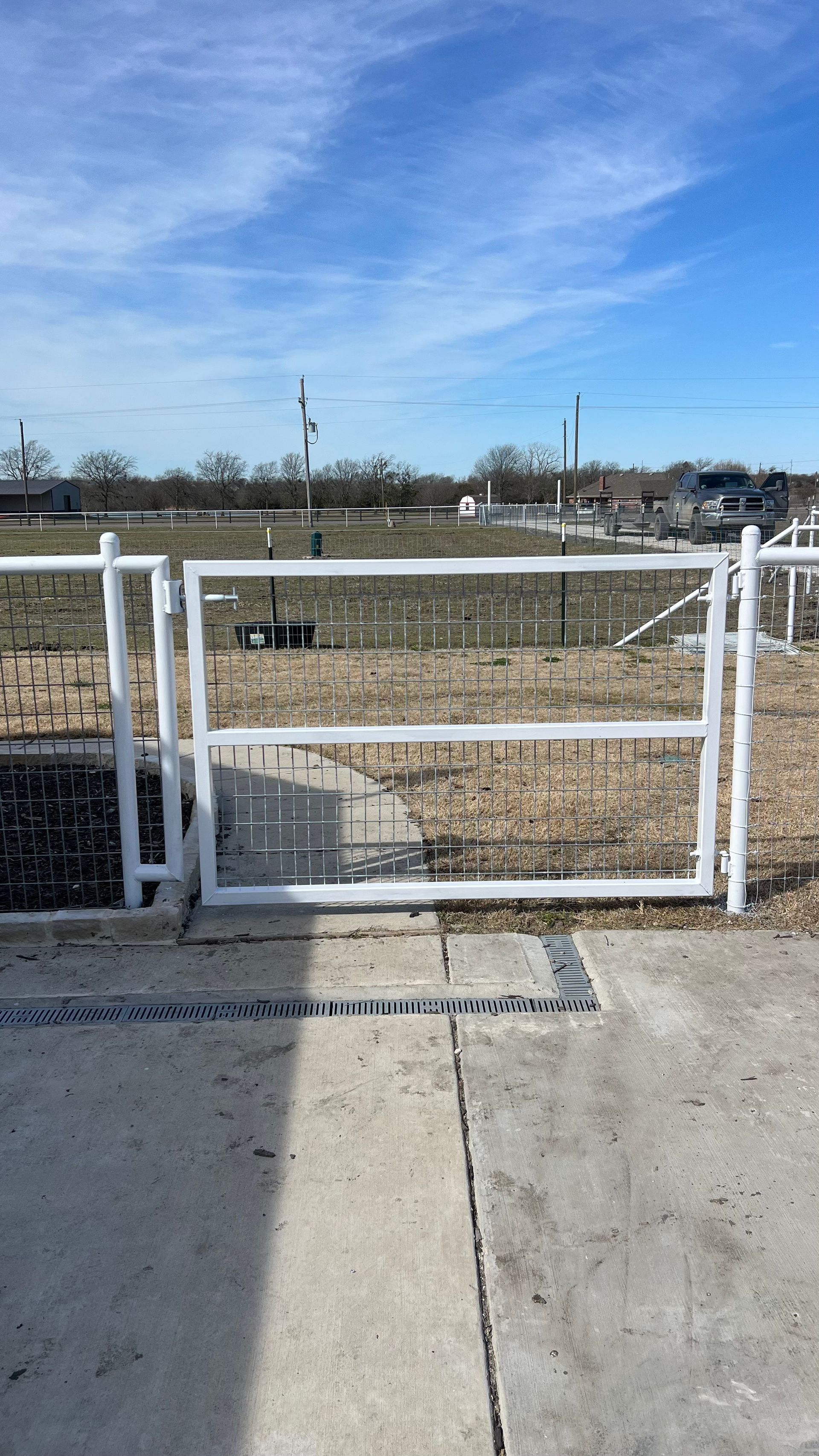 White metal gate in concrete. Background: field and clear, blue sky.