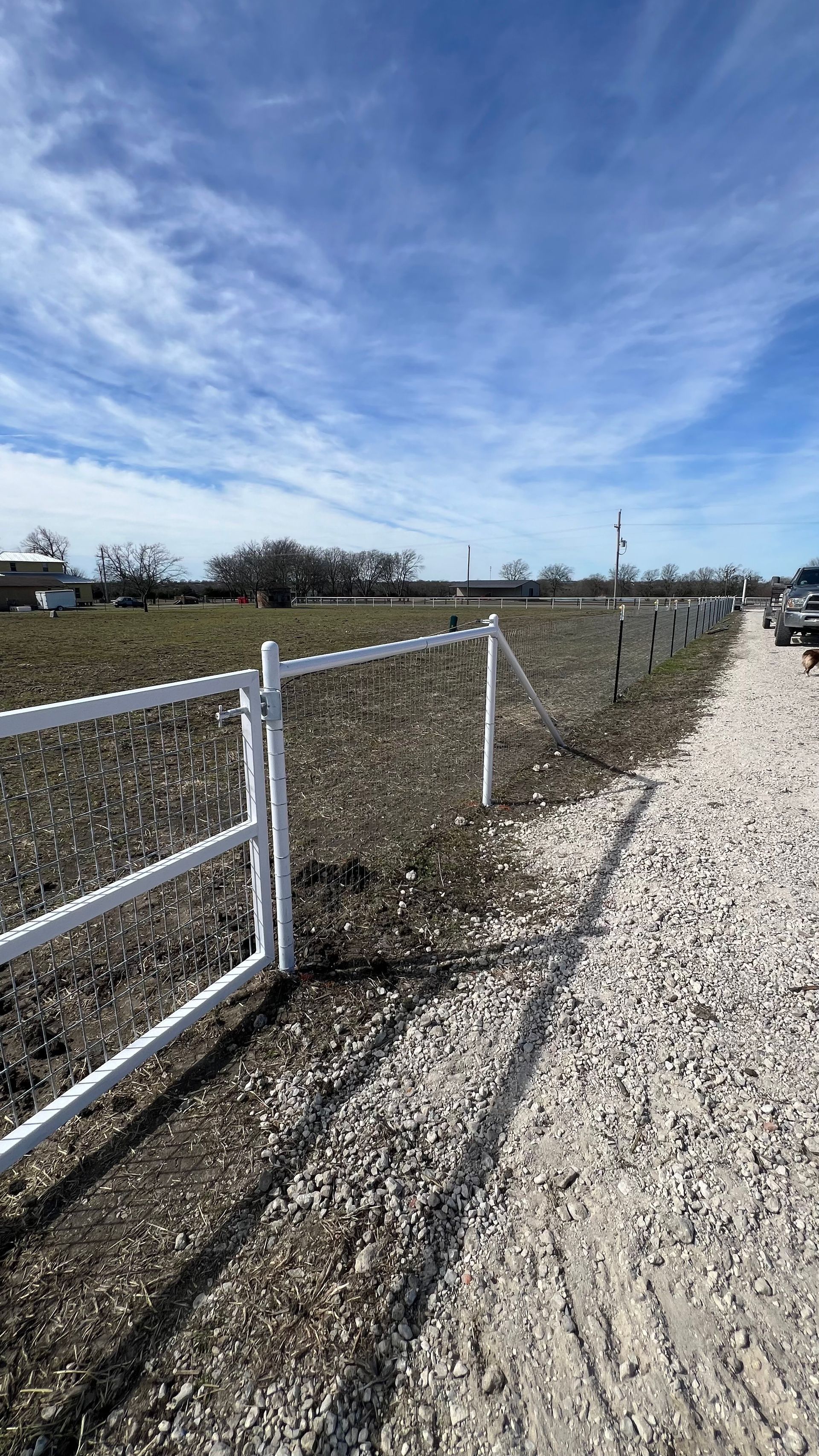 White fenced field with gravel path on a sunny day.