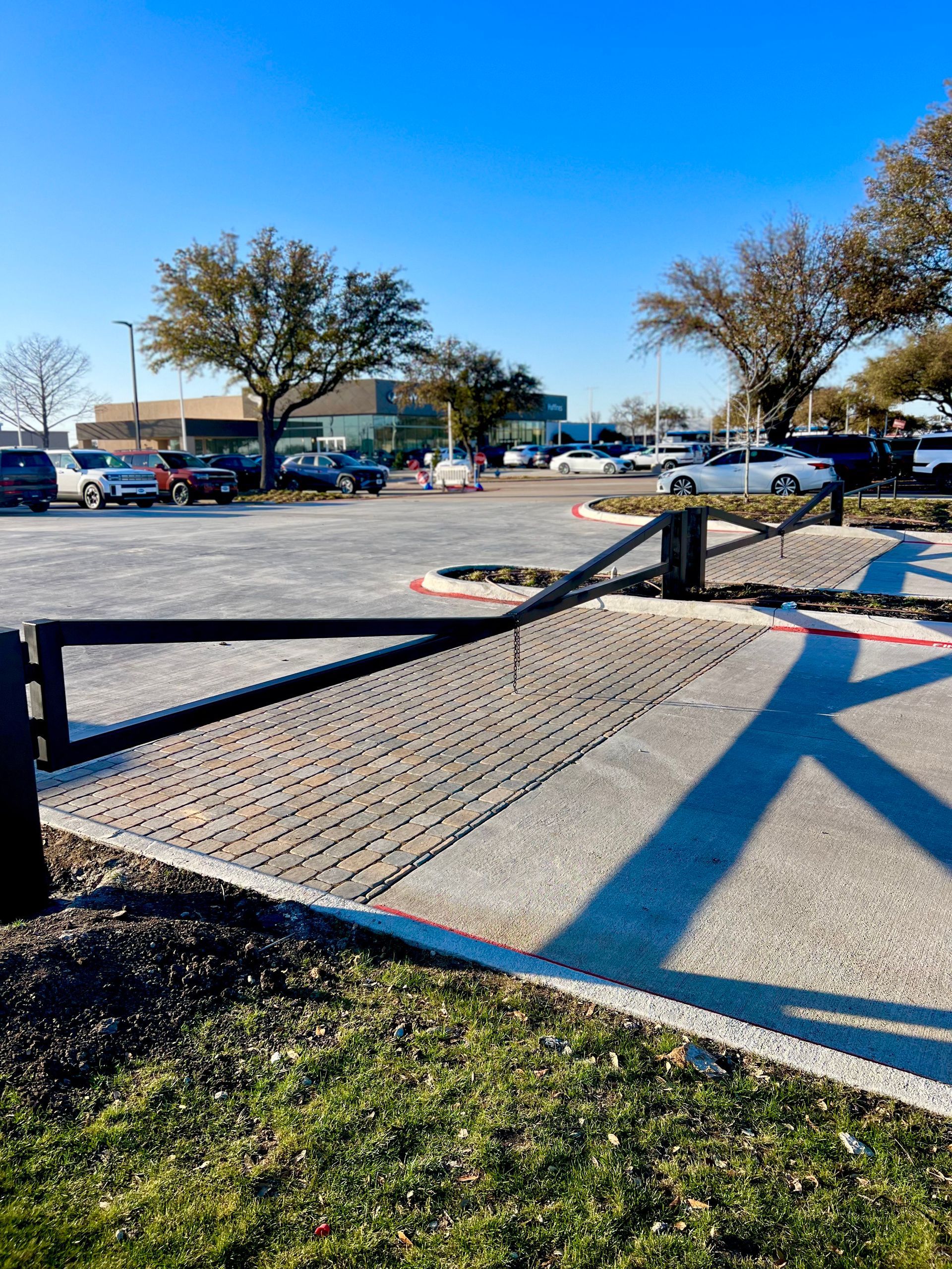 Black gate, gravel path, and parked cars in front of a building under a bright blue sky.
