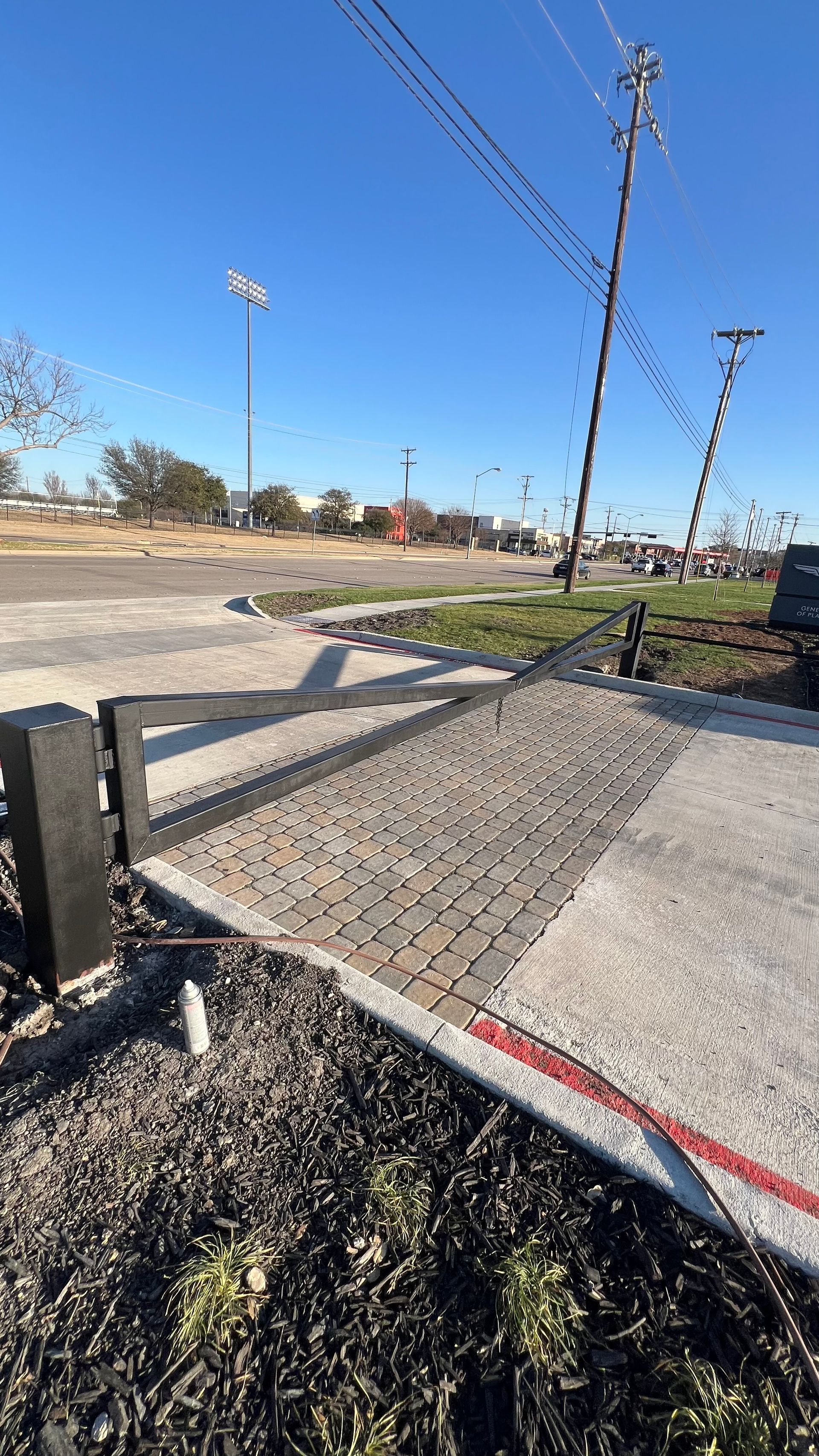 View of a paved walkway, gate, street, and powerlines under a blue sky.
