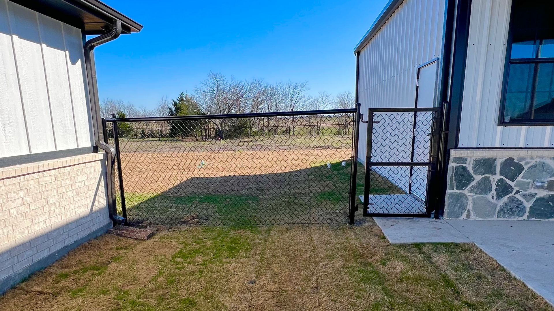 Black metal fence between two buildings, partially open, with a yard beyond.