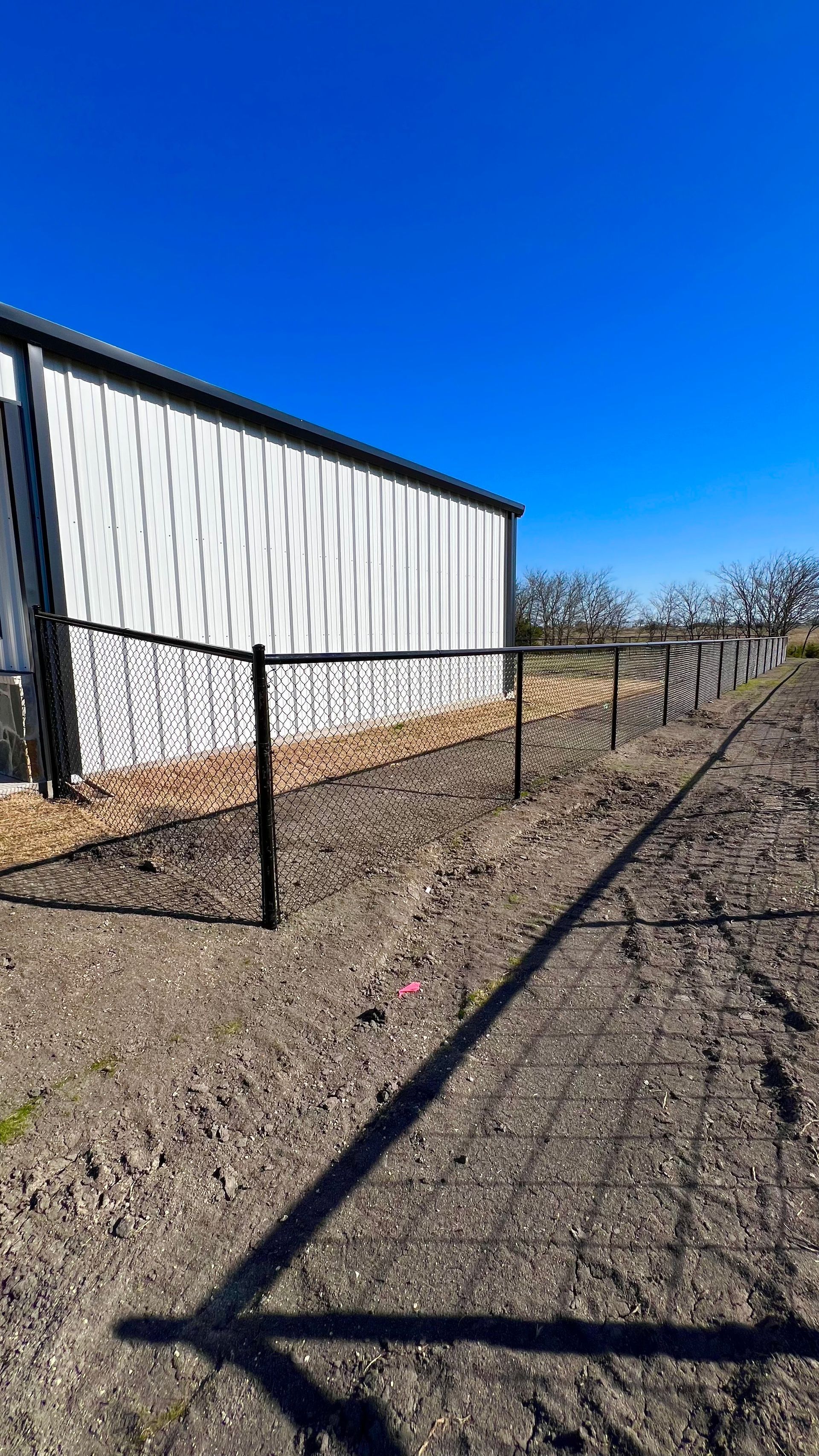 Black metal fence along a building and a vineyard, on a clear day with a bright blue sky.