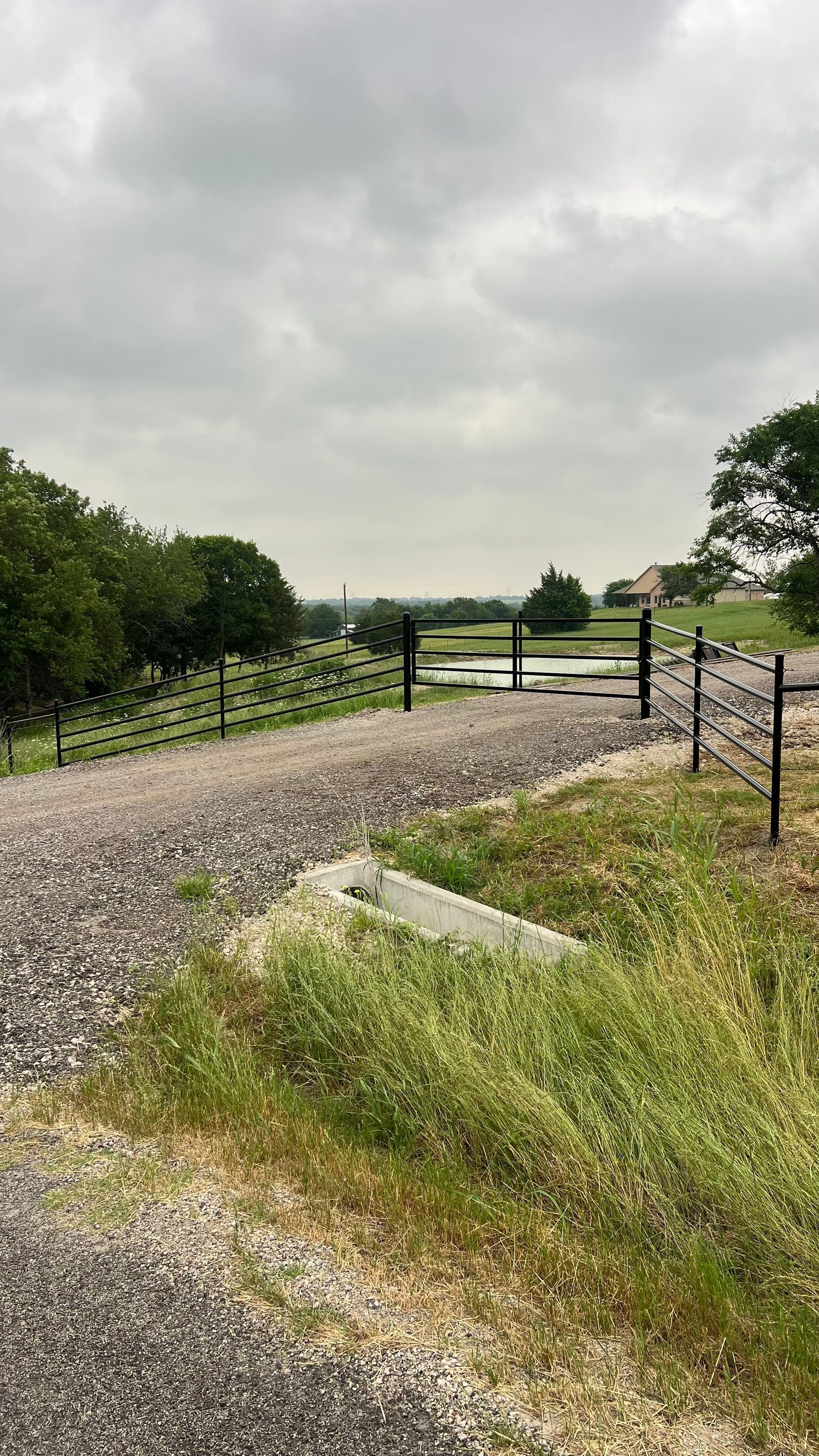 Gravel road leading to a fenced area overlooking a valley under a cloudy sky.
