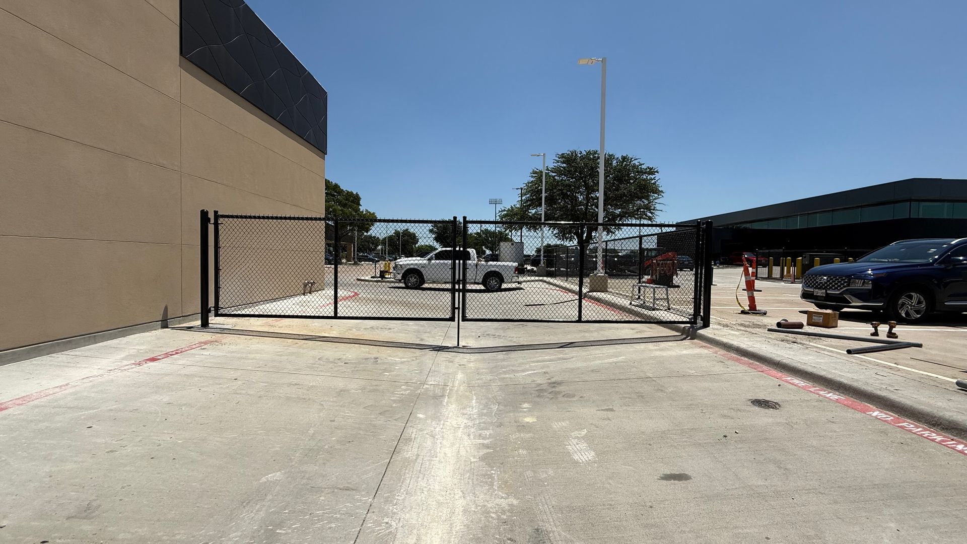 Black security gate blocking access to parking lot, tan building to left, blue sky.