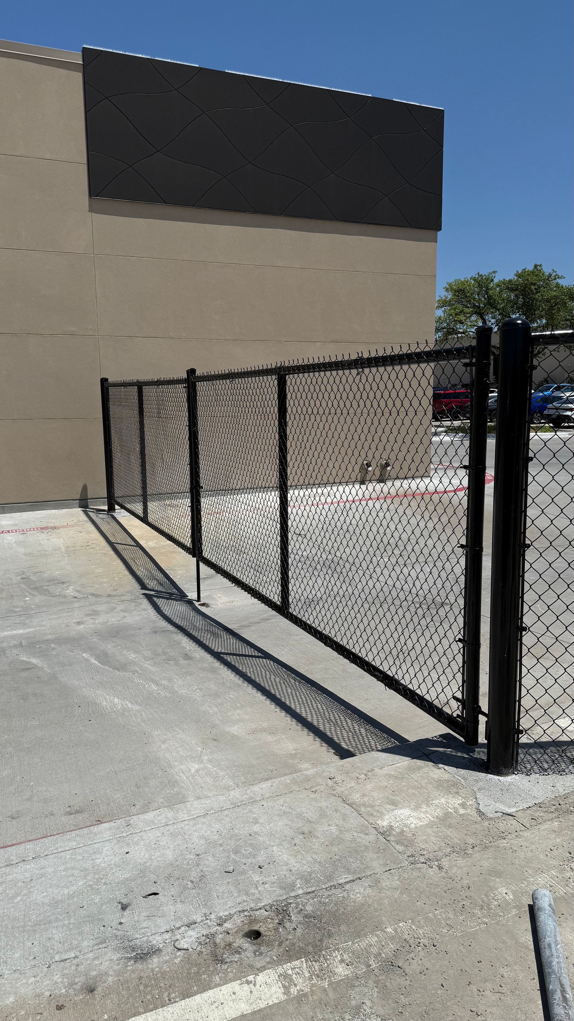 Black chain-link fence bordering a building's side, with concrete ground.