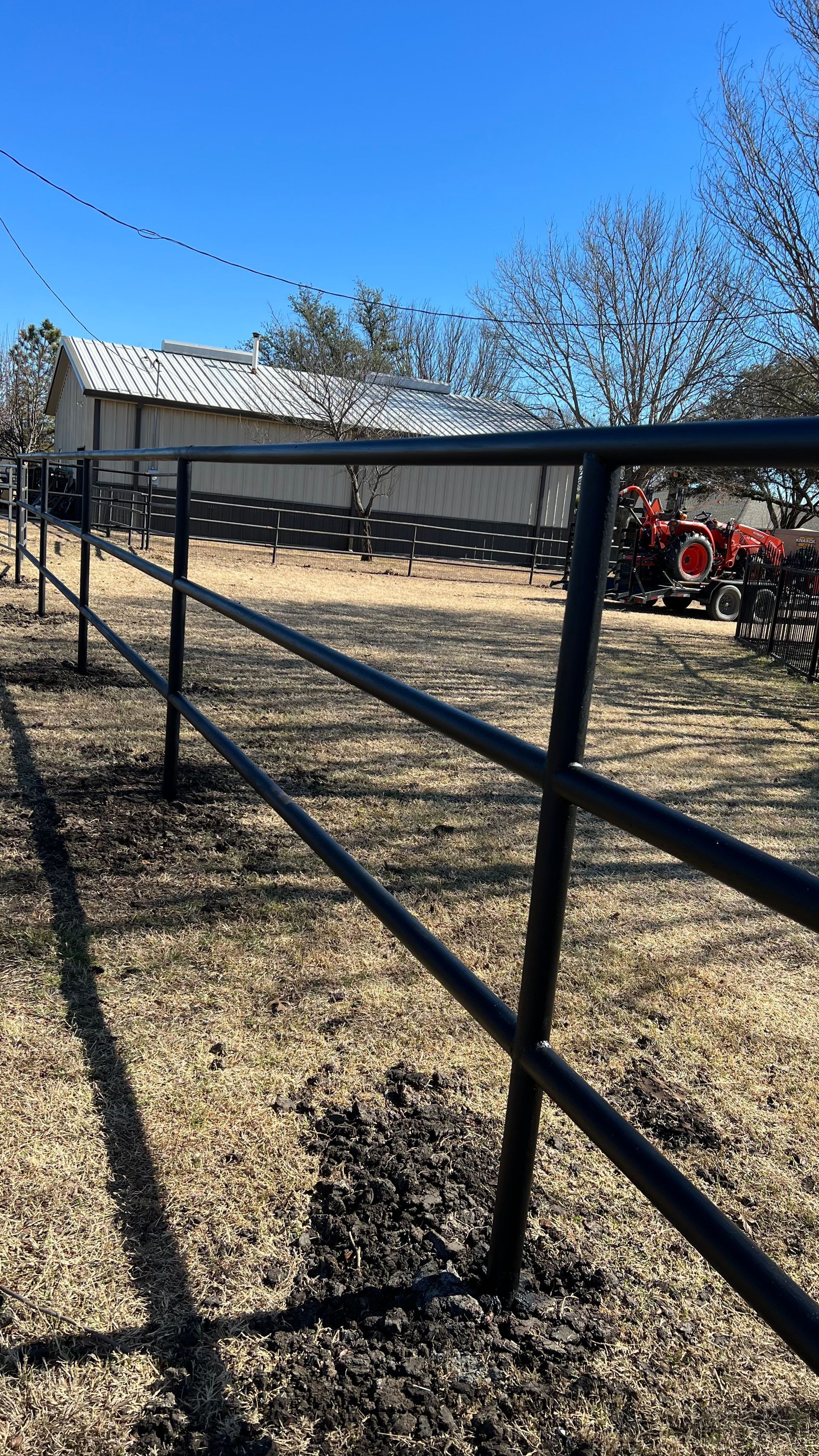 A black metal fence surrounds a dirt field with a tractor in the background.