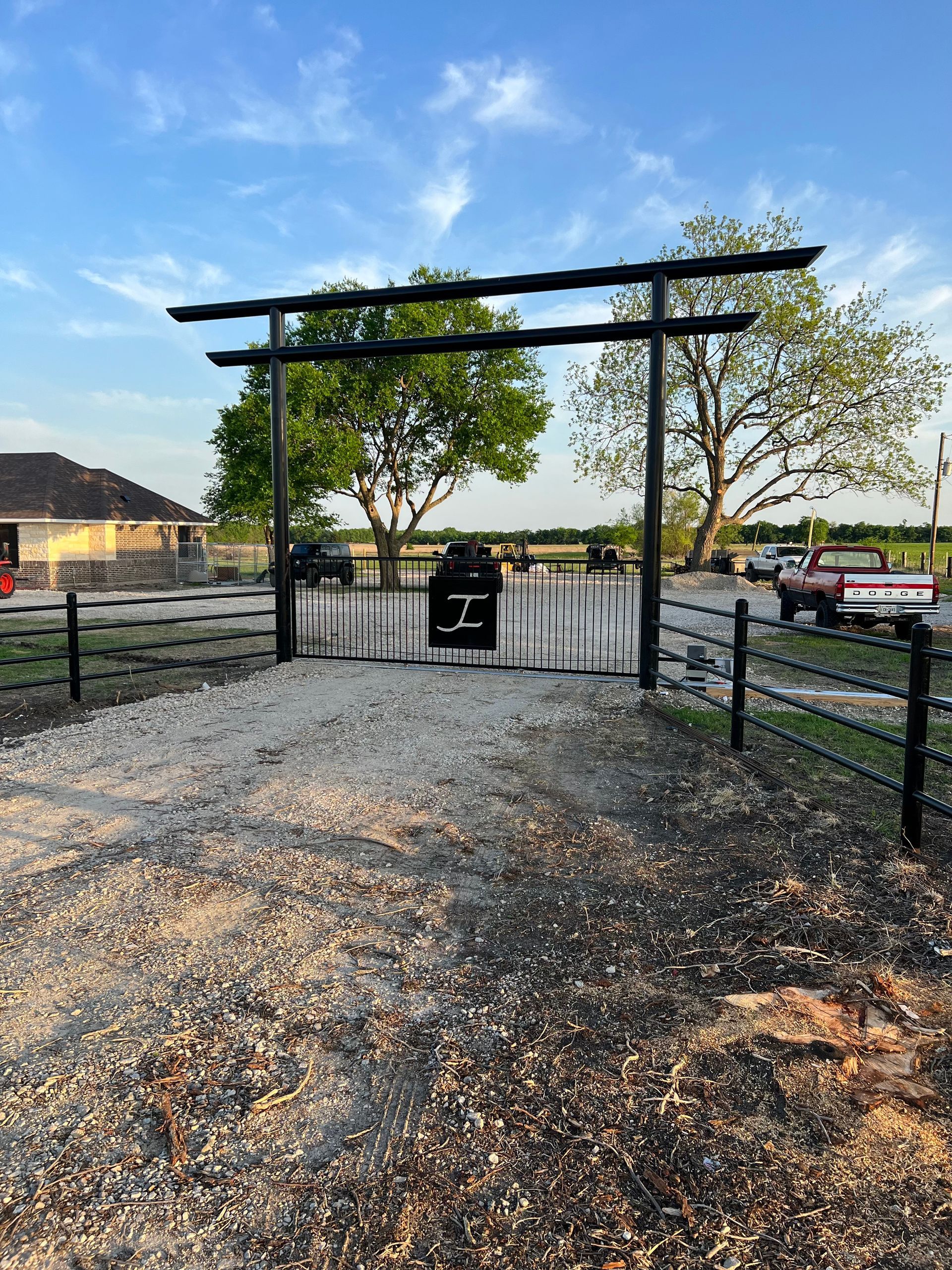 A fence with a gate in the middle of a gravel road.