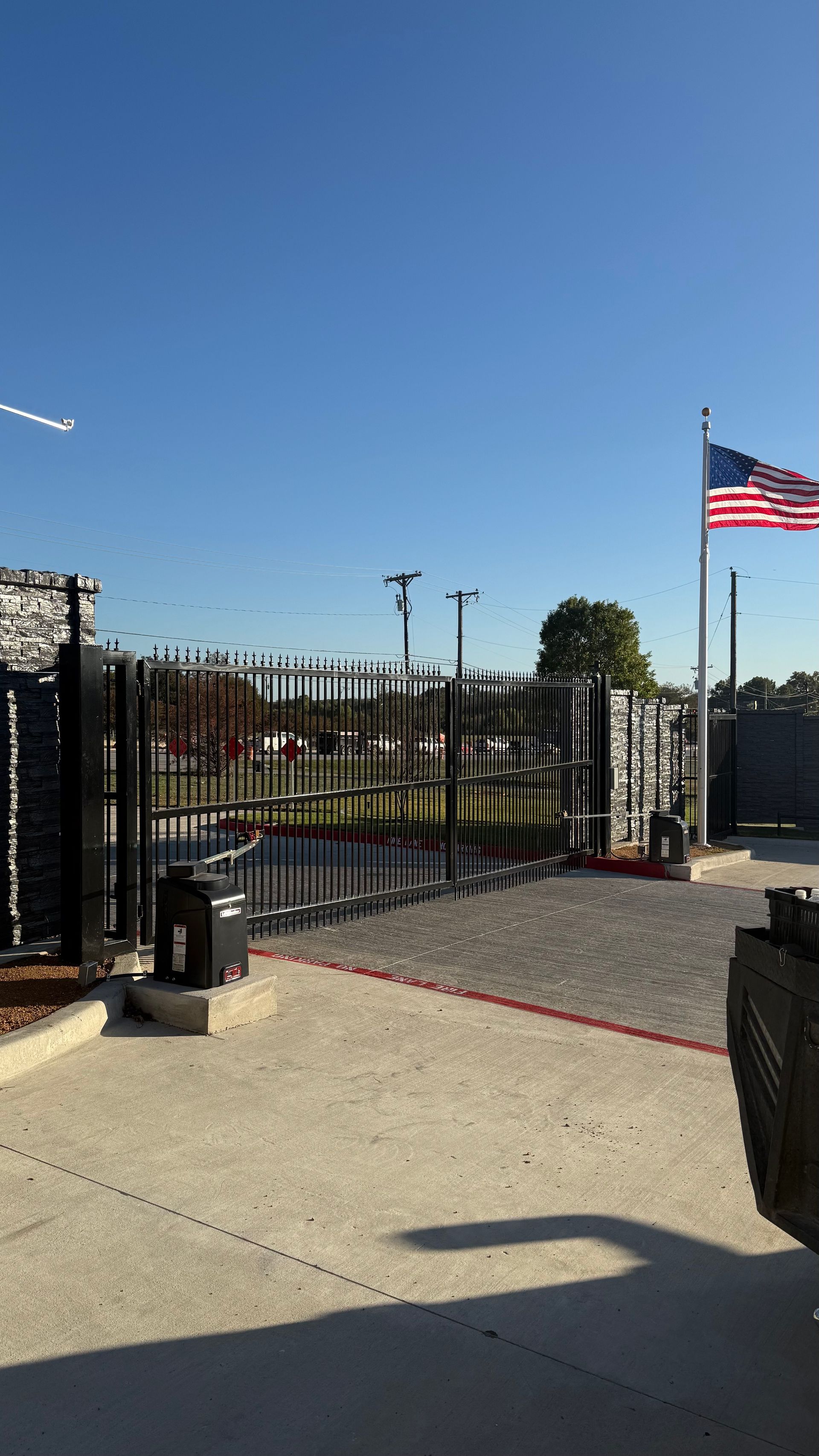 A black gate with an American flag flying in front of a blue sky.