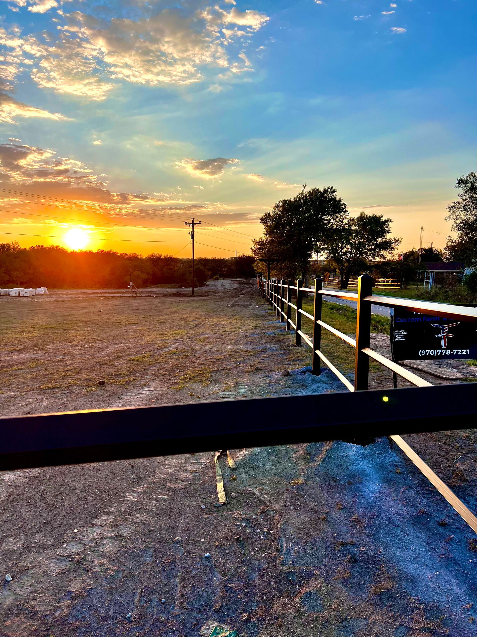 A fence along a dirt road with a sunset in the background.