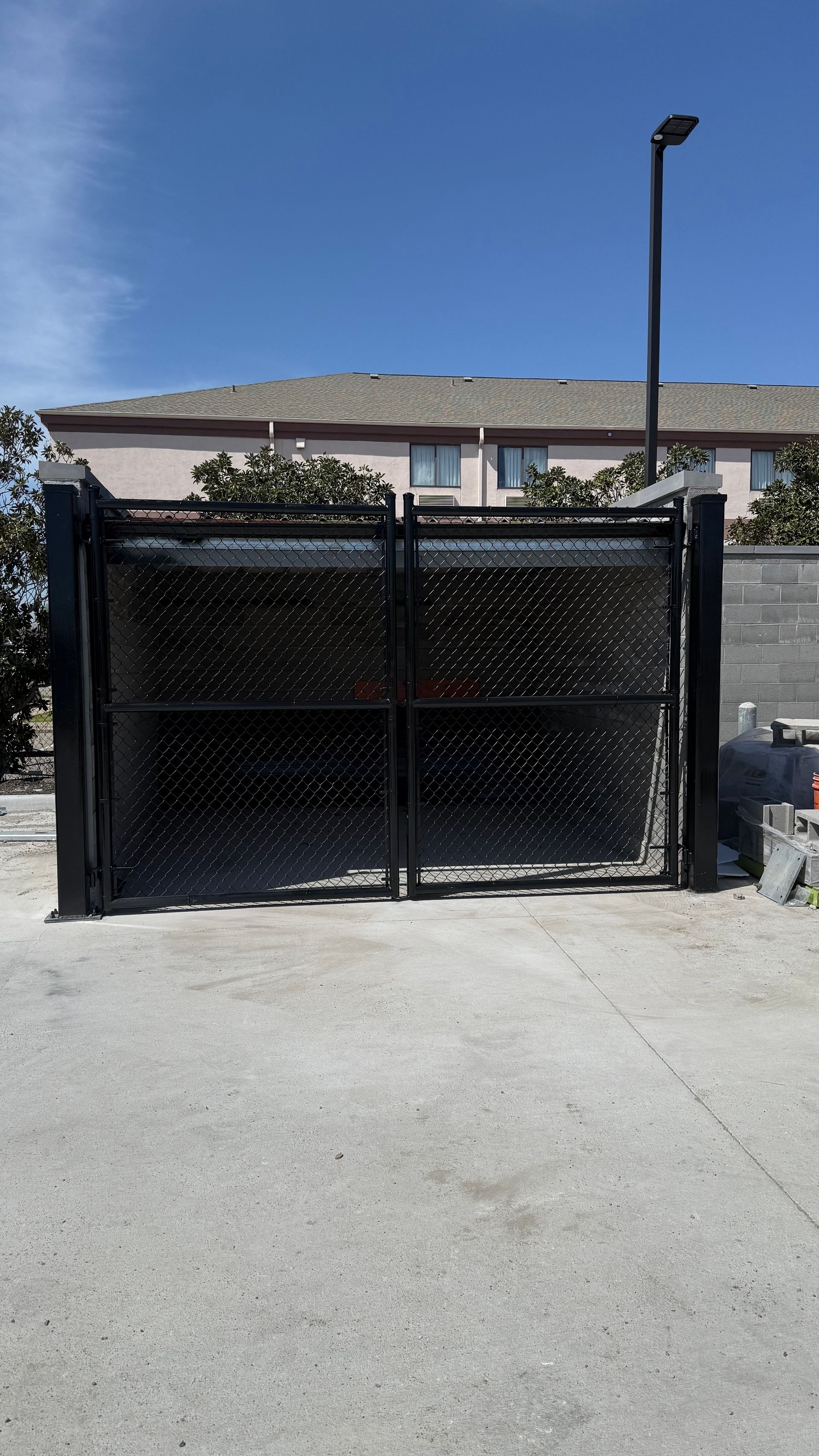 A black metal gate with a perforated pattern stands against a building under a clear blue sky.
