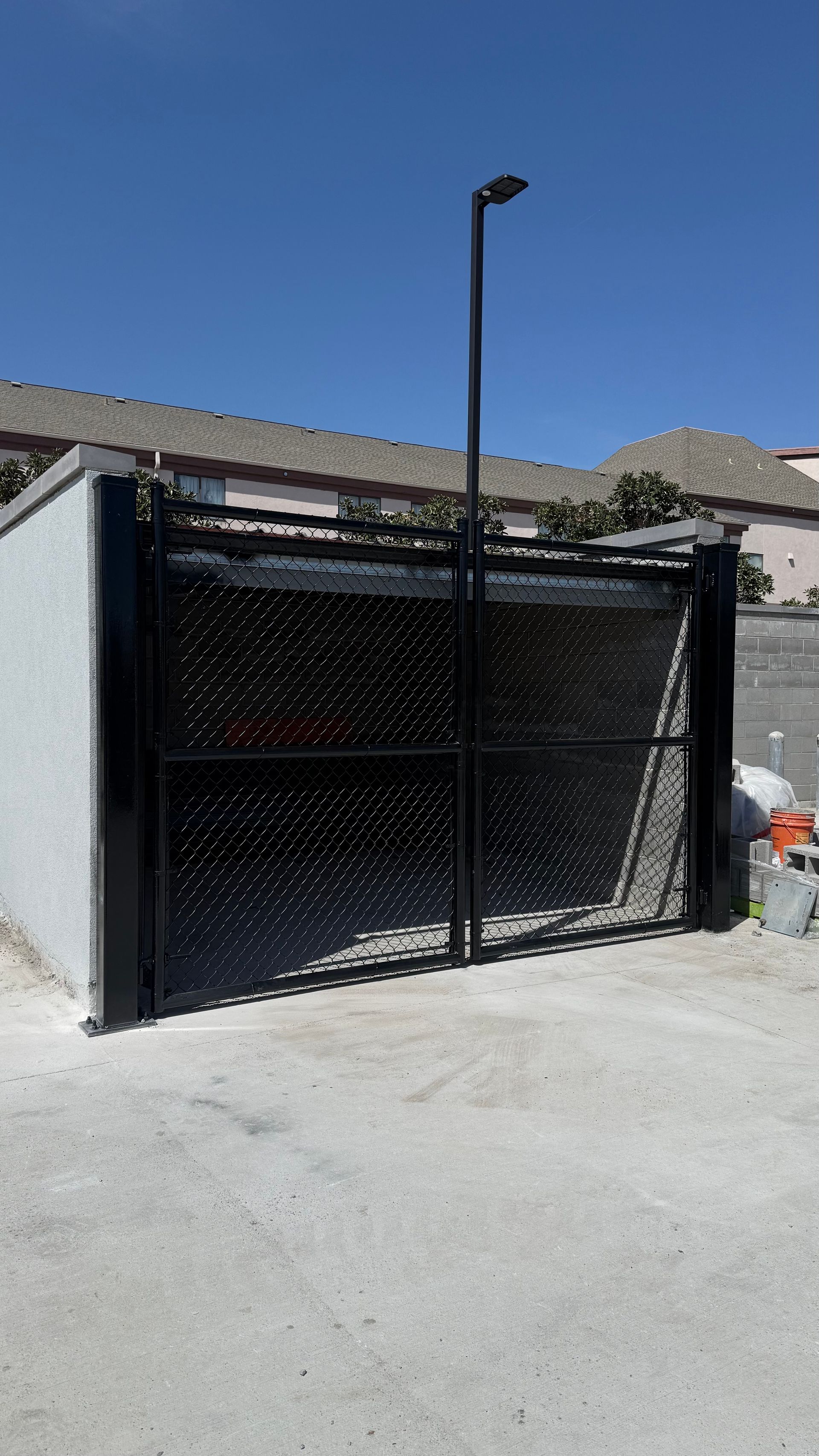 A black metal gate with a decorative, perforated pattern stands in front of a concrete wall under a clear blue sky.