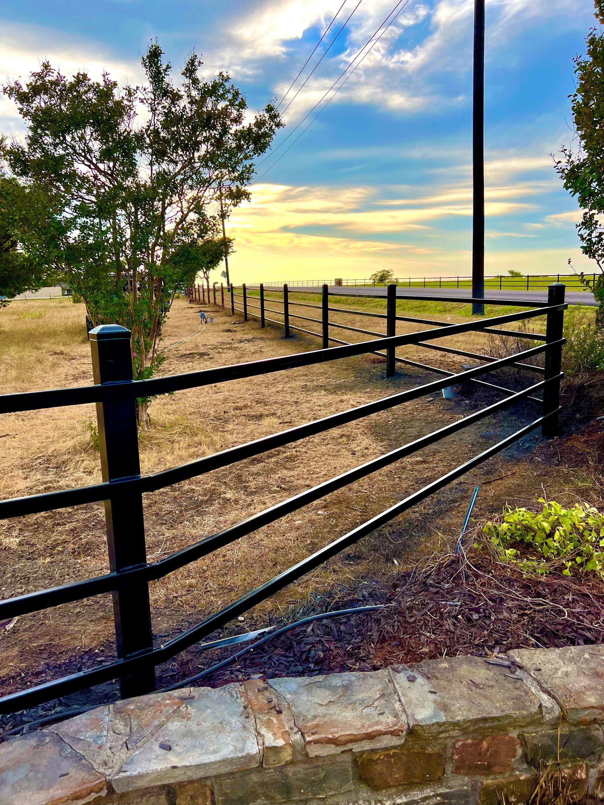 A black fence surrounds a dirt road in a field.