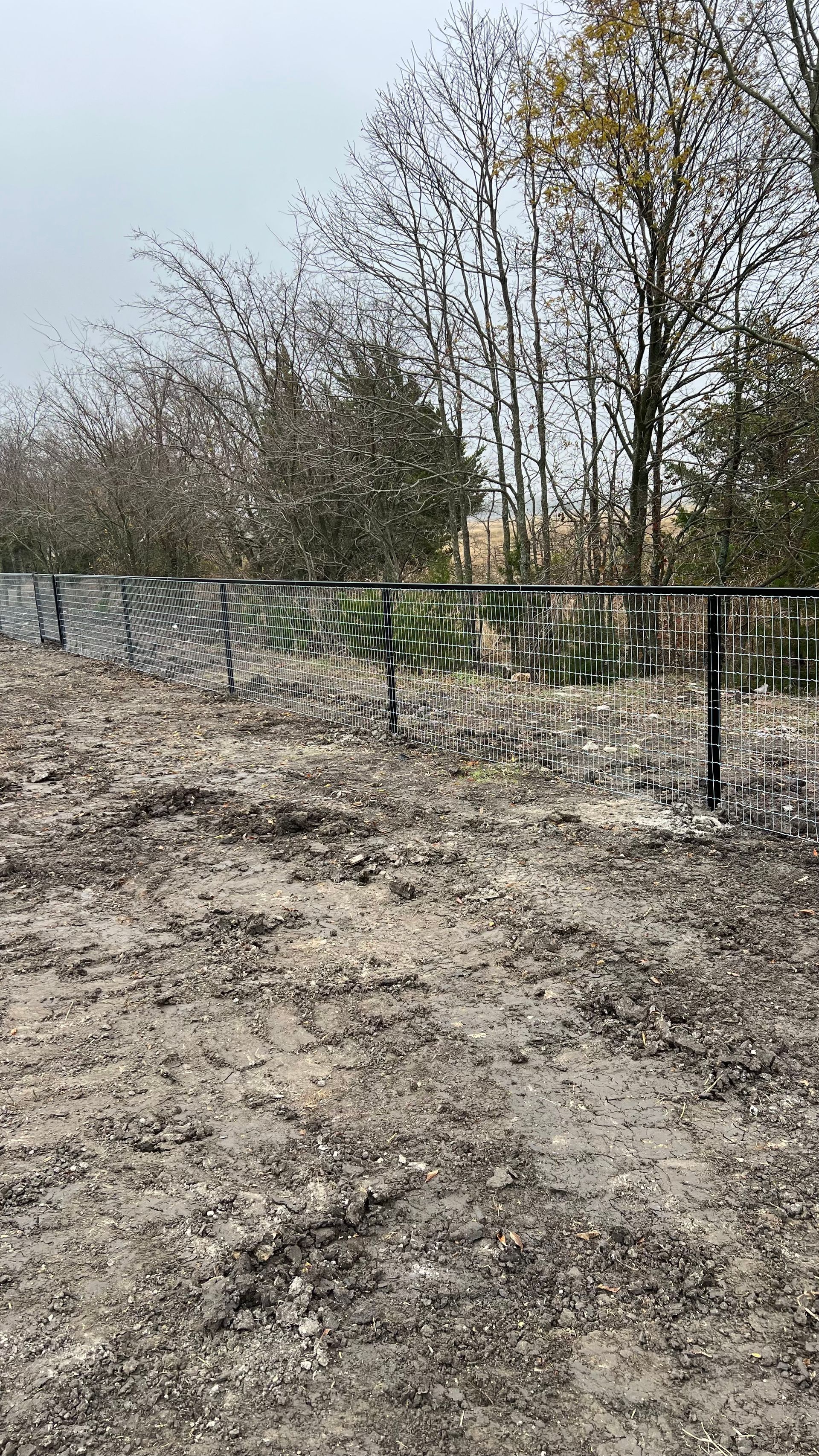 A fence is surrounding a dirt field with trees in the background.