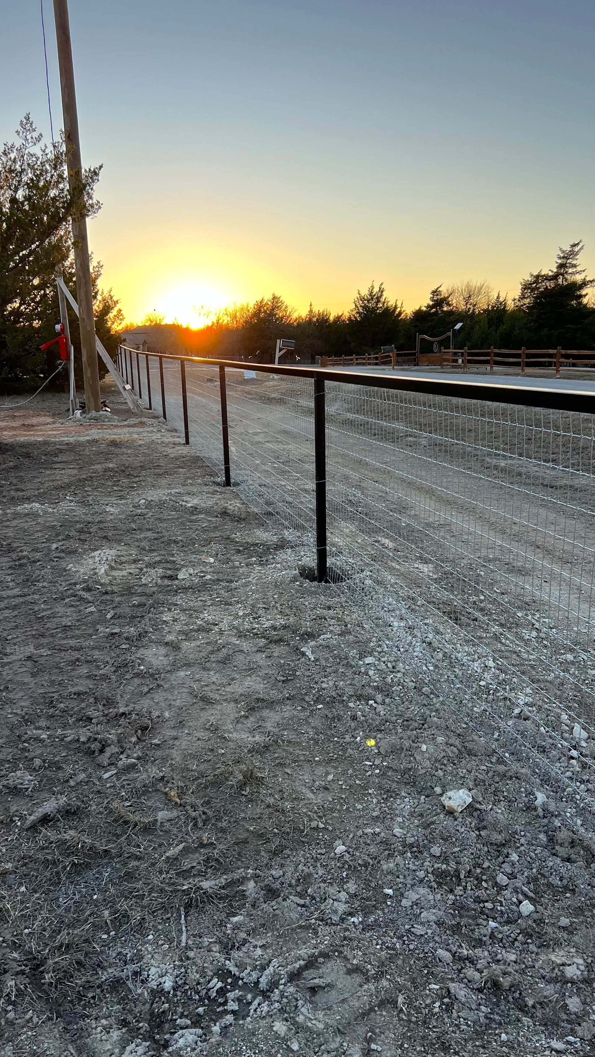 A sunset over a dirt field with a railing in the foreground.