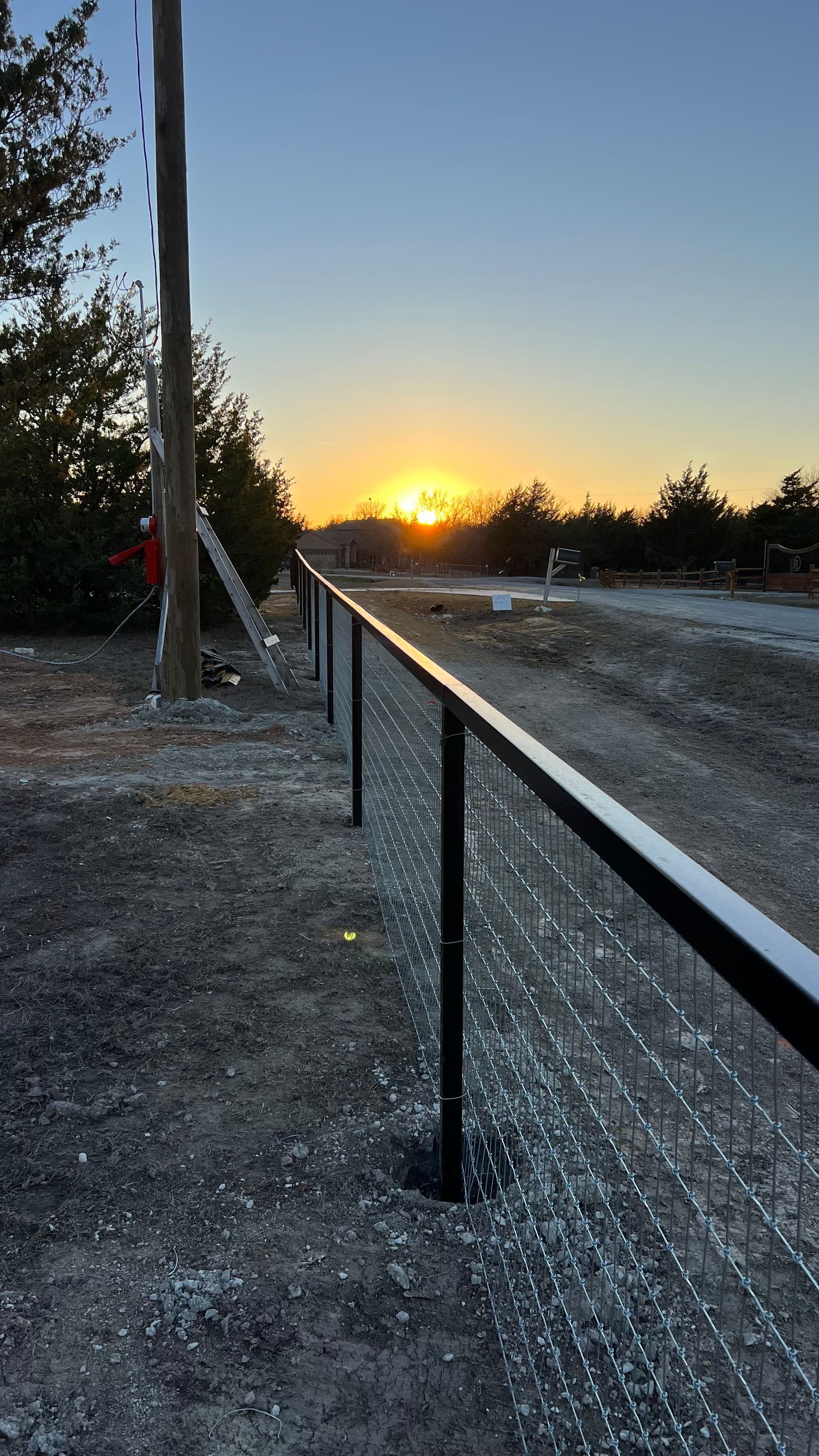 The sun is setting behind a barbed wire fence.