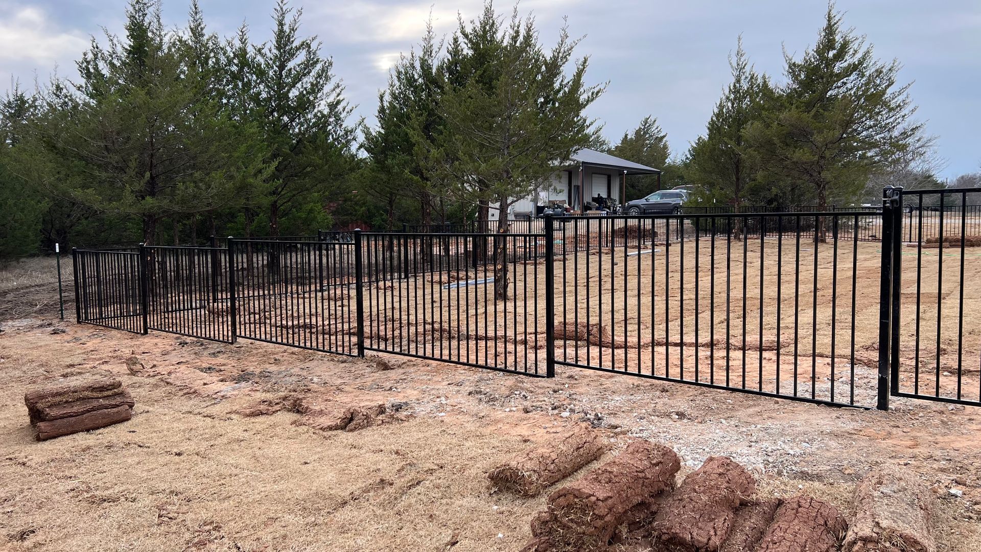 There is a fence in the middle of a field with trees in the background.