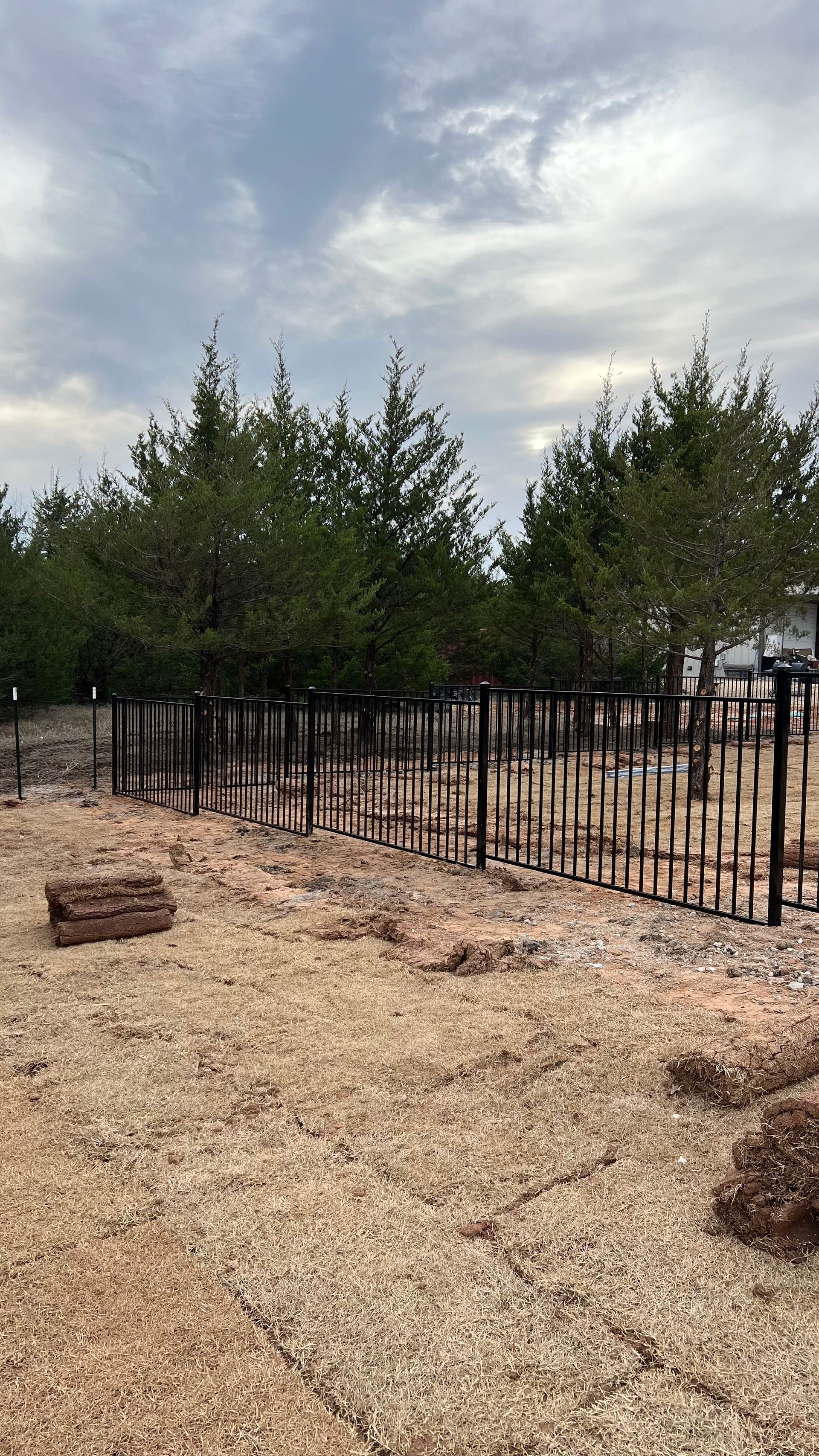 There is a fence in the middle of a field with trees in the background.