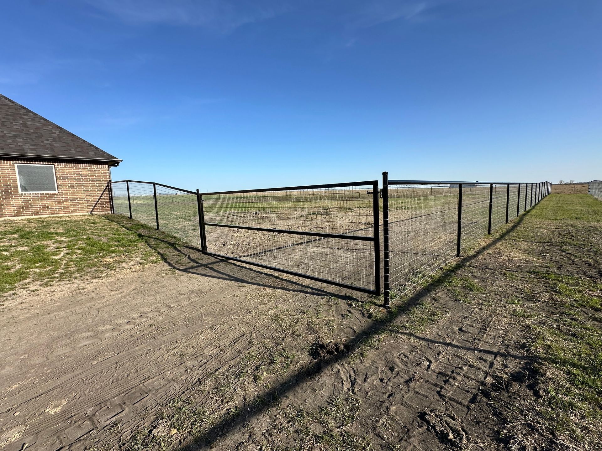 Black metal fence with gate in a field next to a small building under a blue sky.