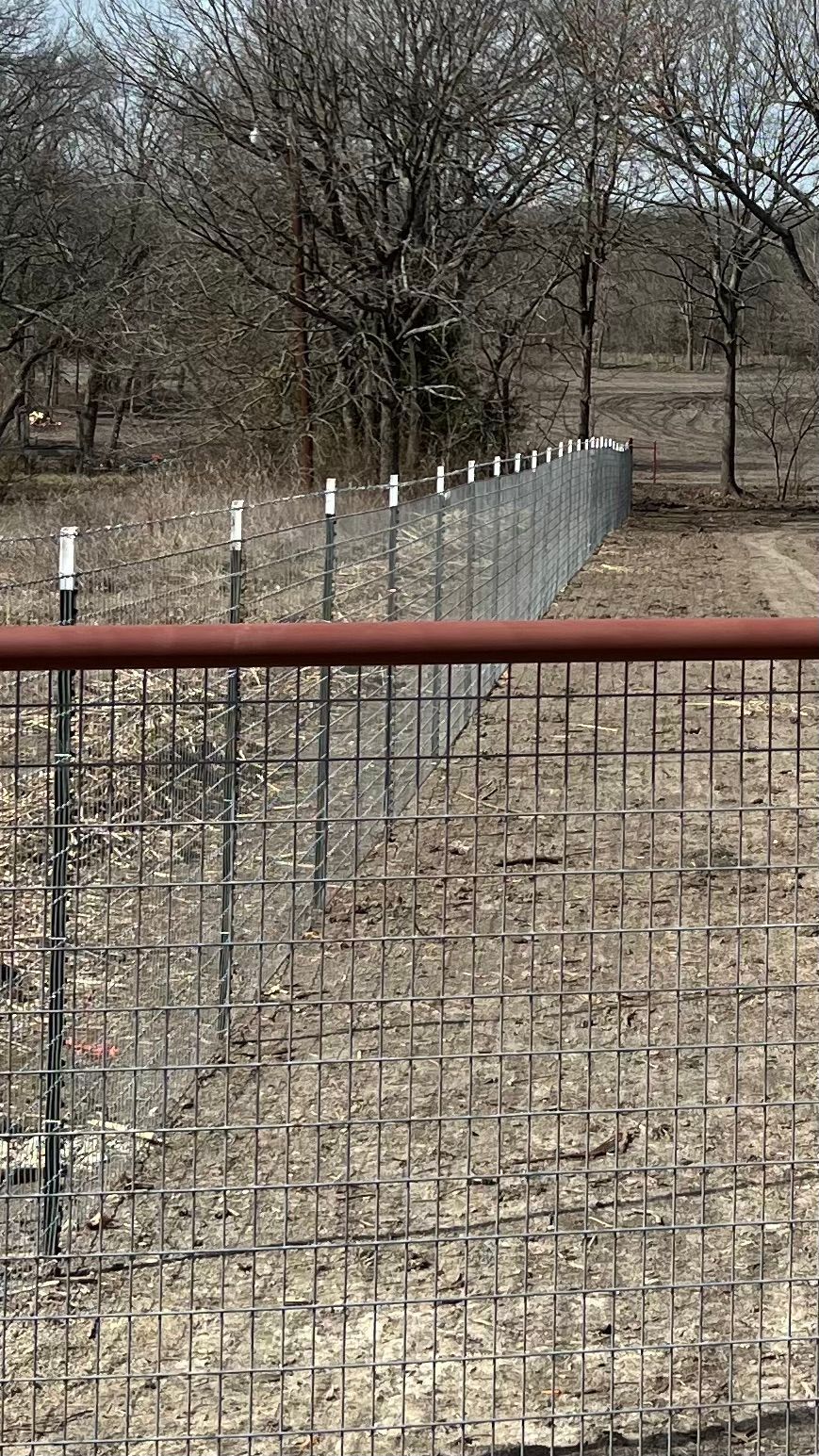 A fence is surrounding a field with trees in the background.