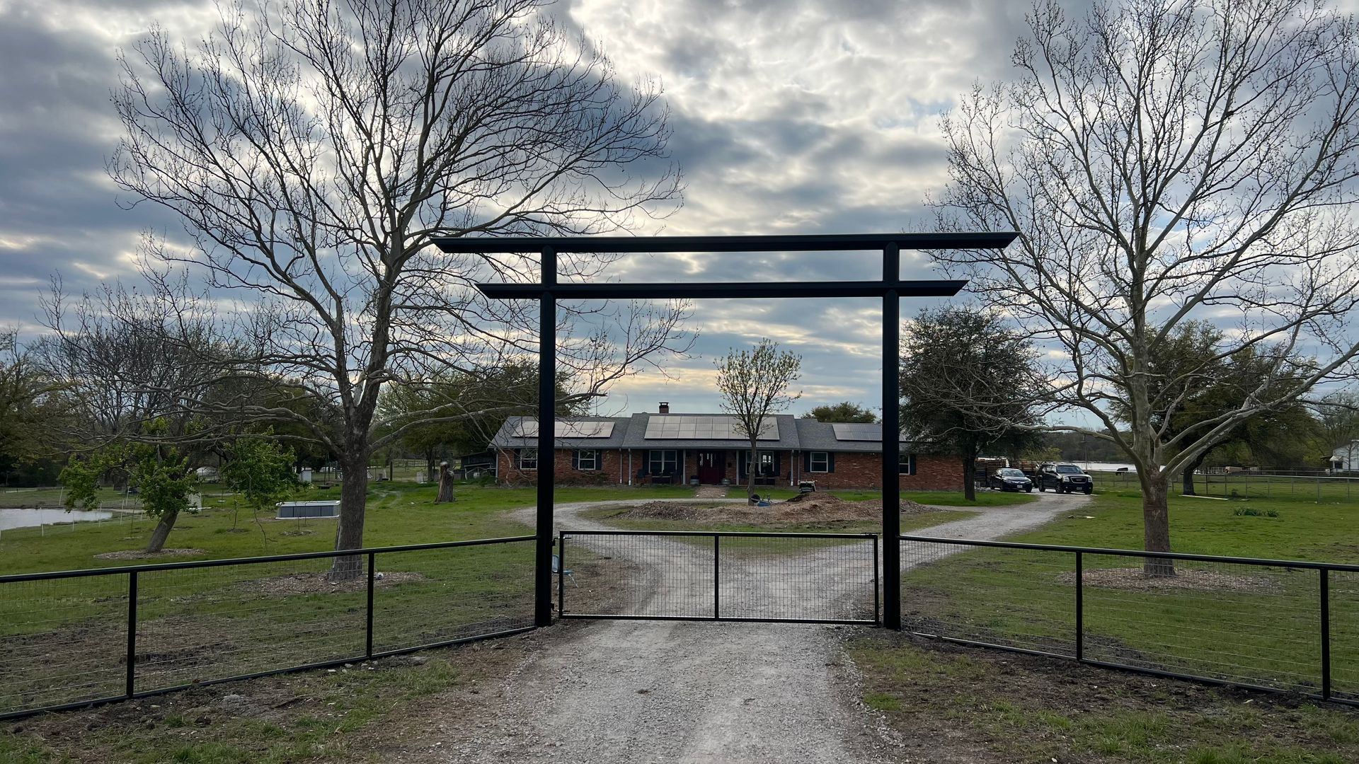 There is a gate in the middle of a dirt road leading to a house.