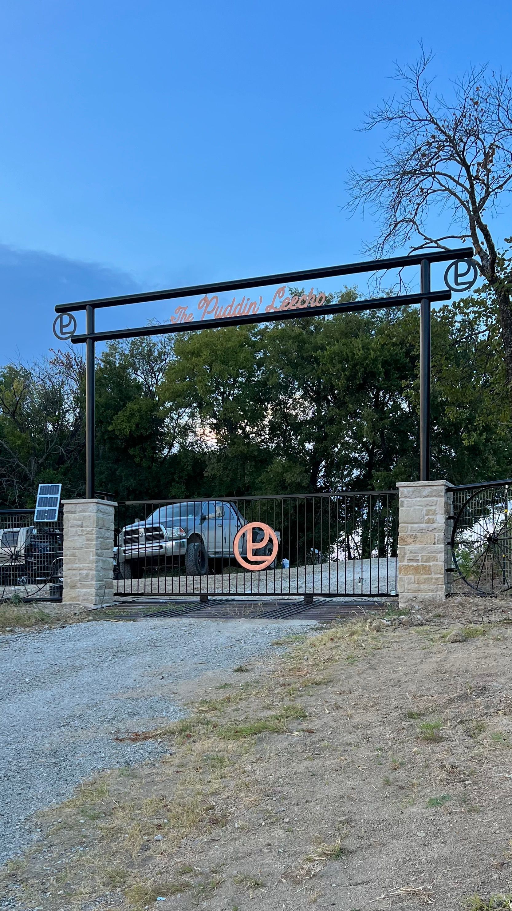 A metal gate with a sign on it is surrounded by trees and gravel.
