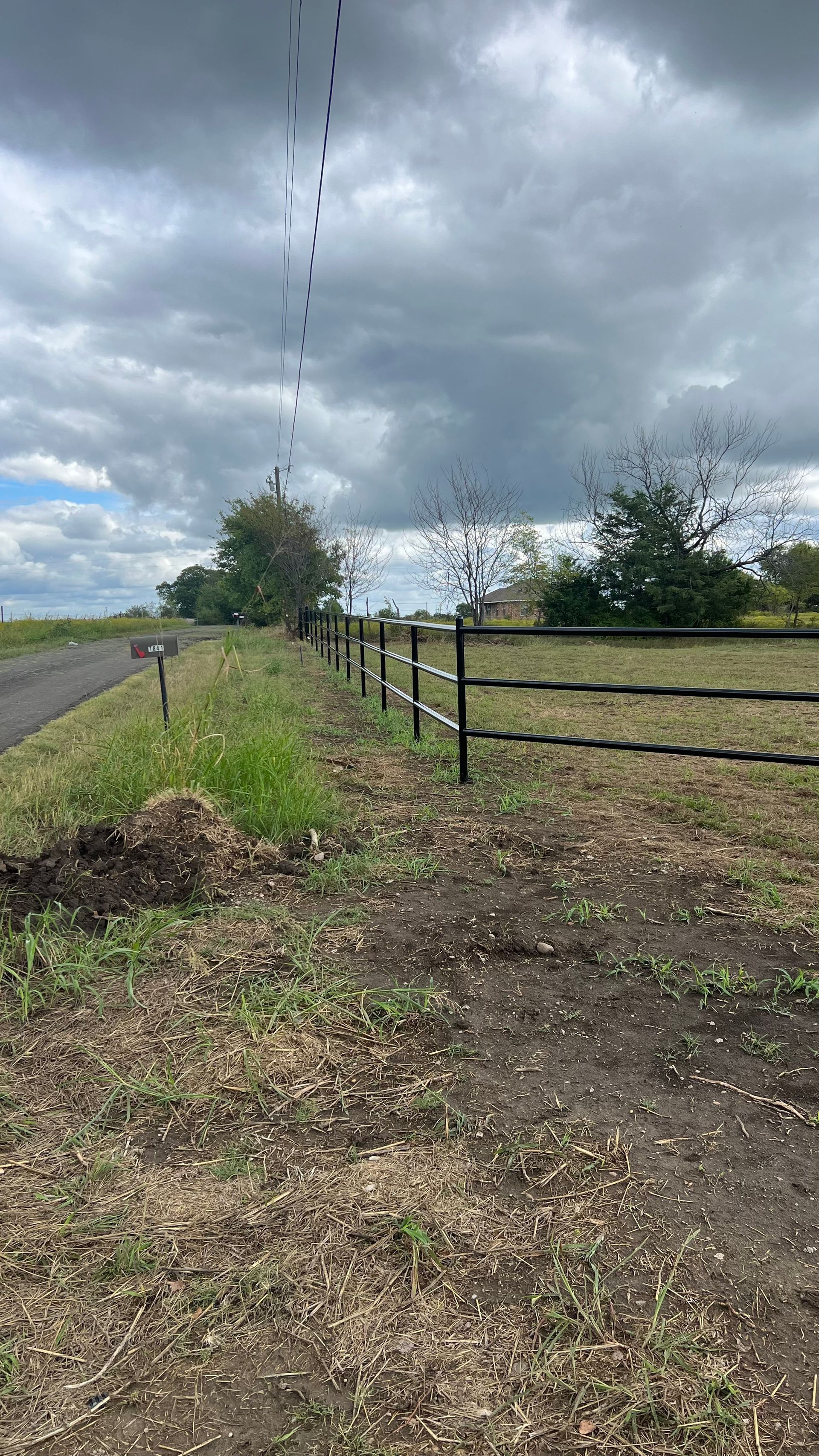 A fence surrounds a field next to a road on a cloudy day.