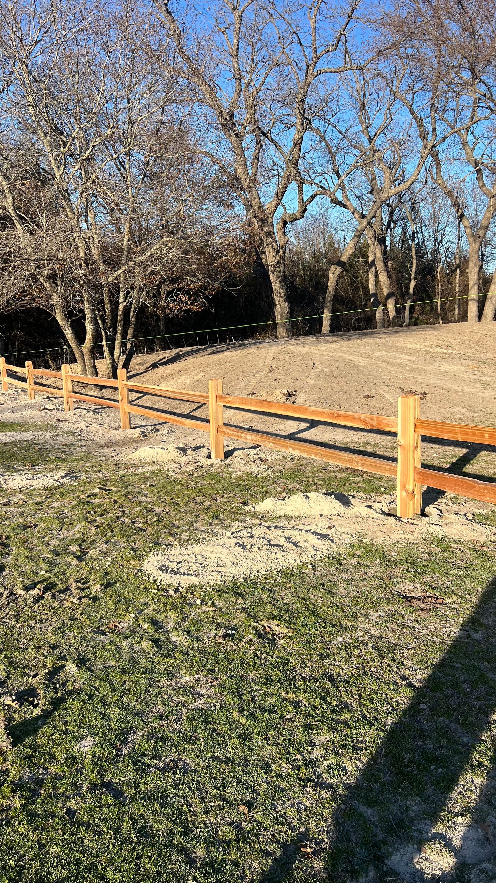 A wooden fence surrounds a grassy field with trees in the background.