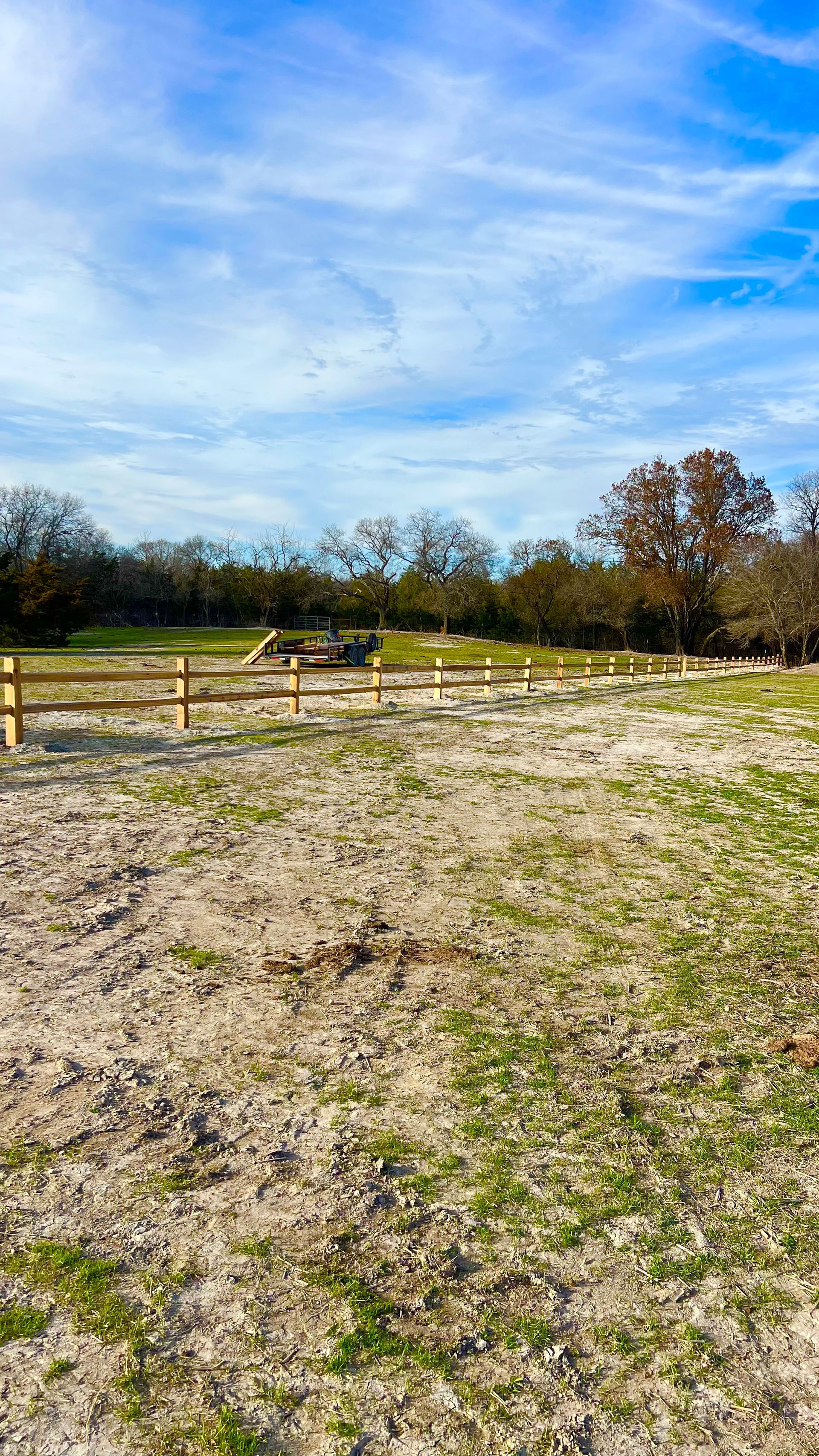 A field with a wooden fence and trees in the background on a sunny day.