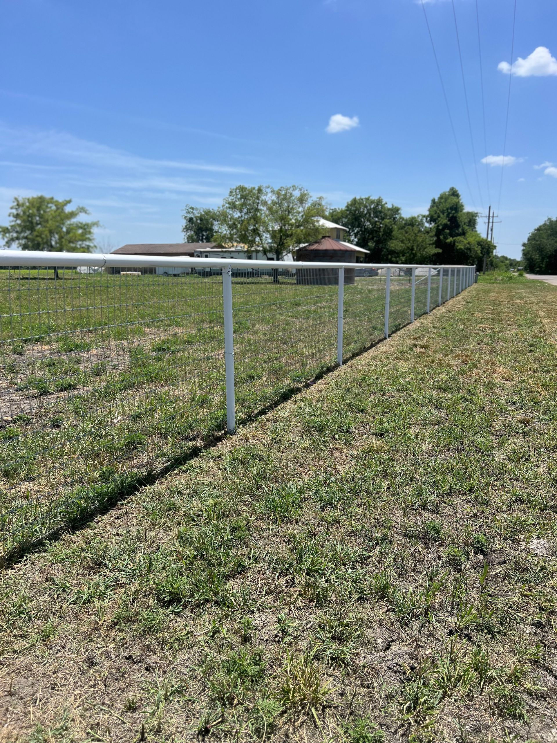 A fence surrounds a grassy field with a house in the background.