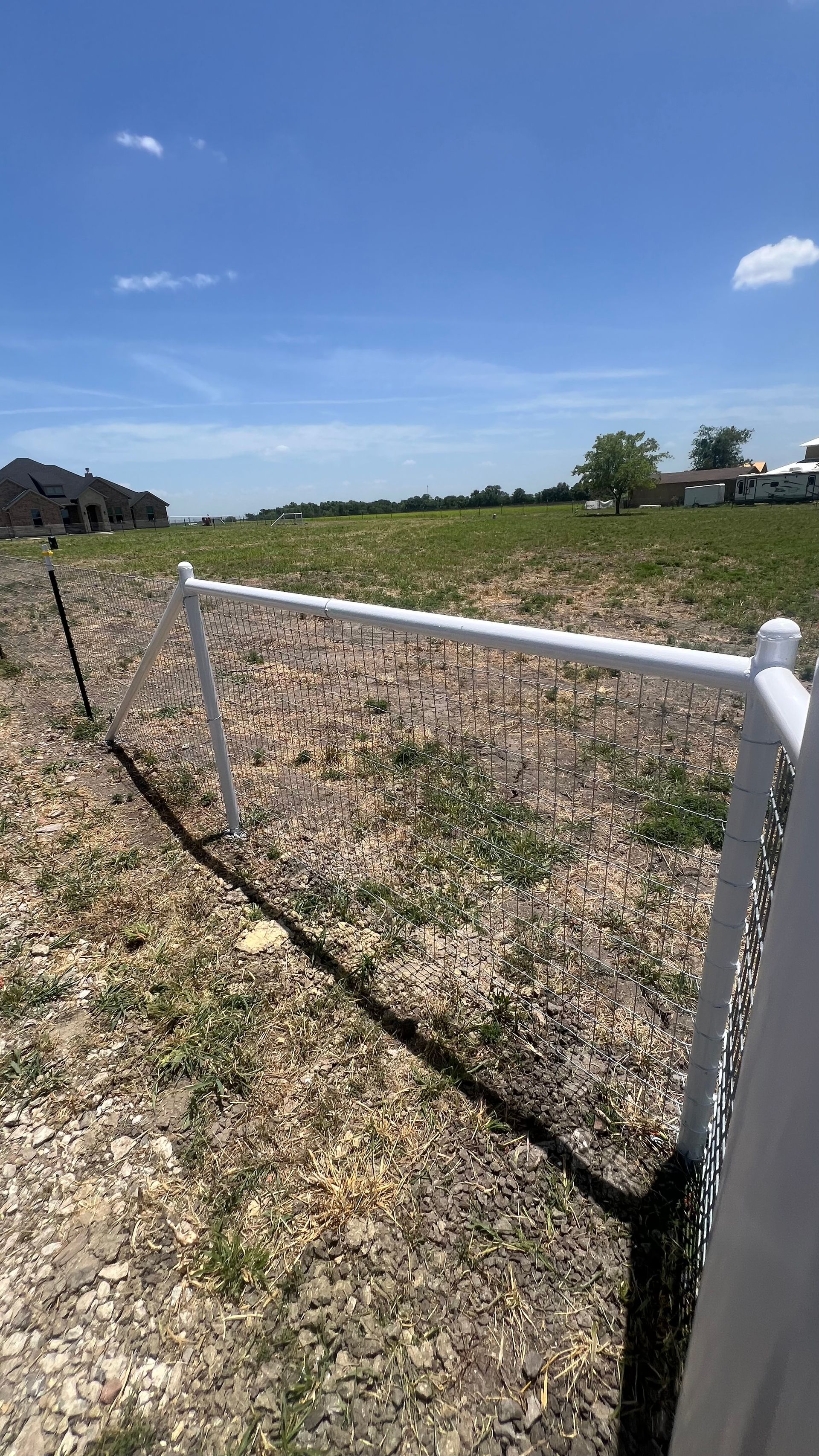 A white fence surrounds a field with a house in the background.