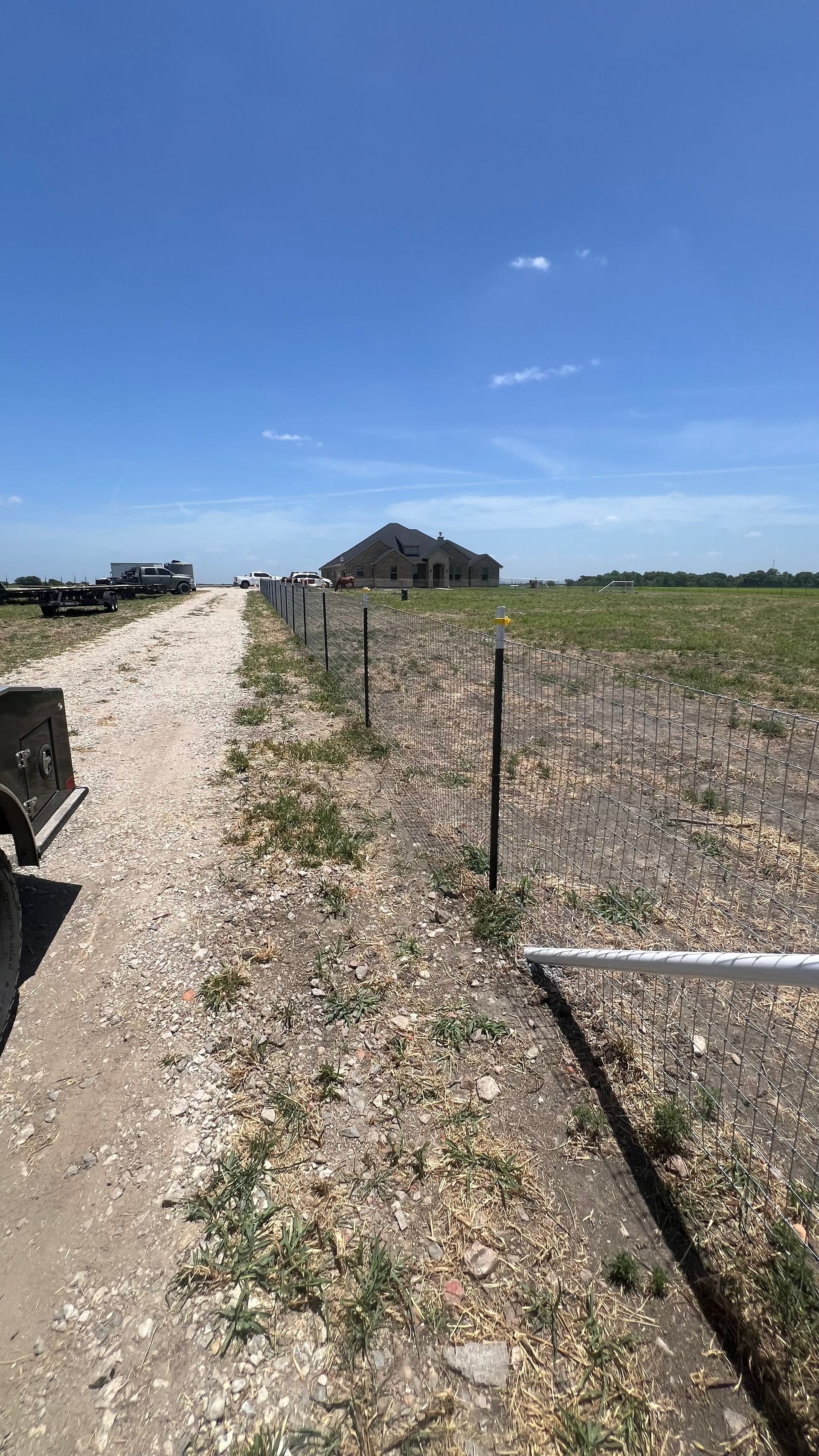A dirt road with a fence and a house in the background.
