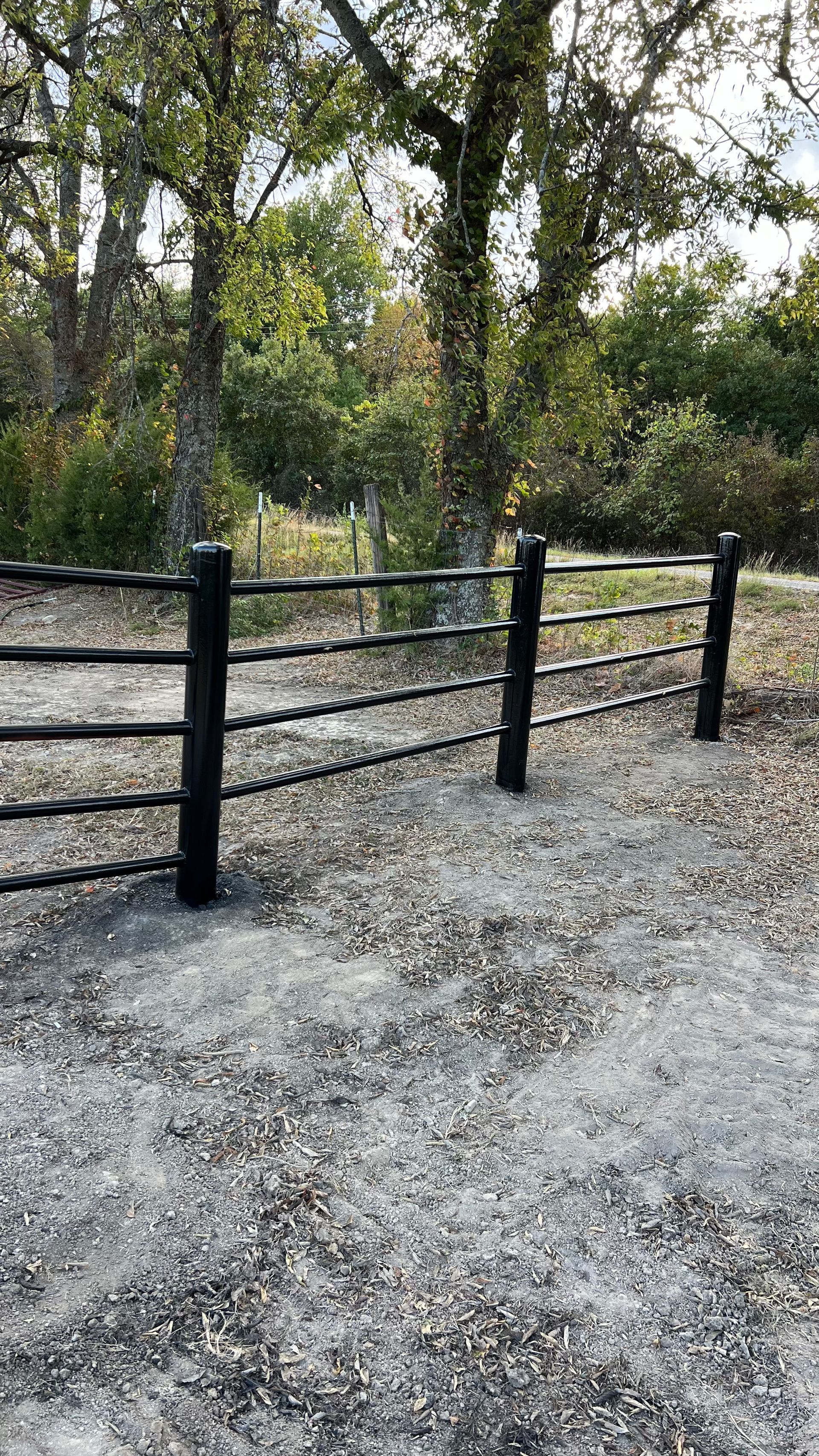 A black fence is surrounded by gravel and trees in a park.