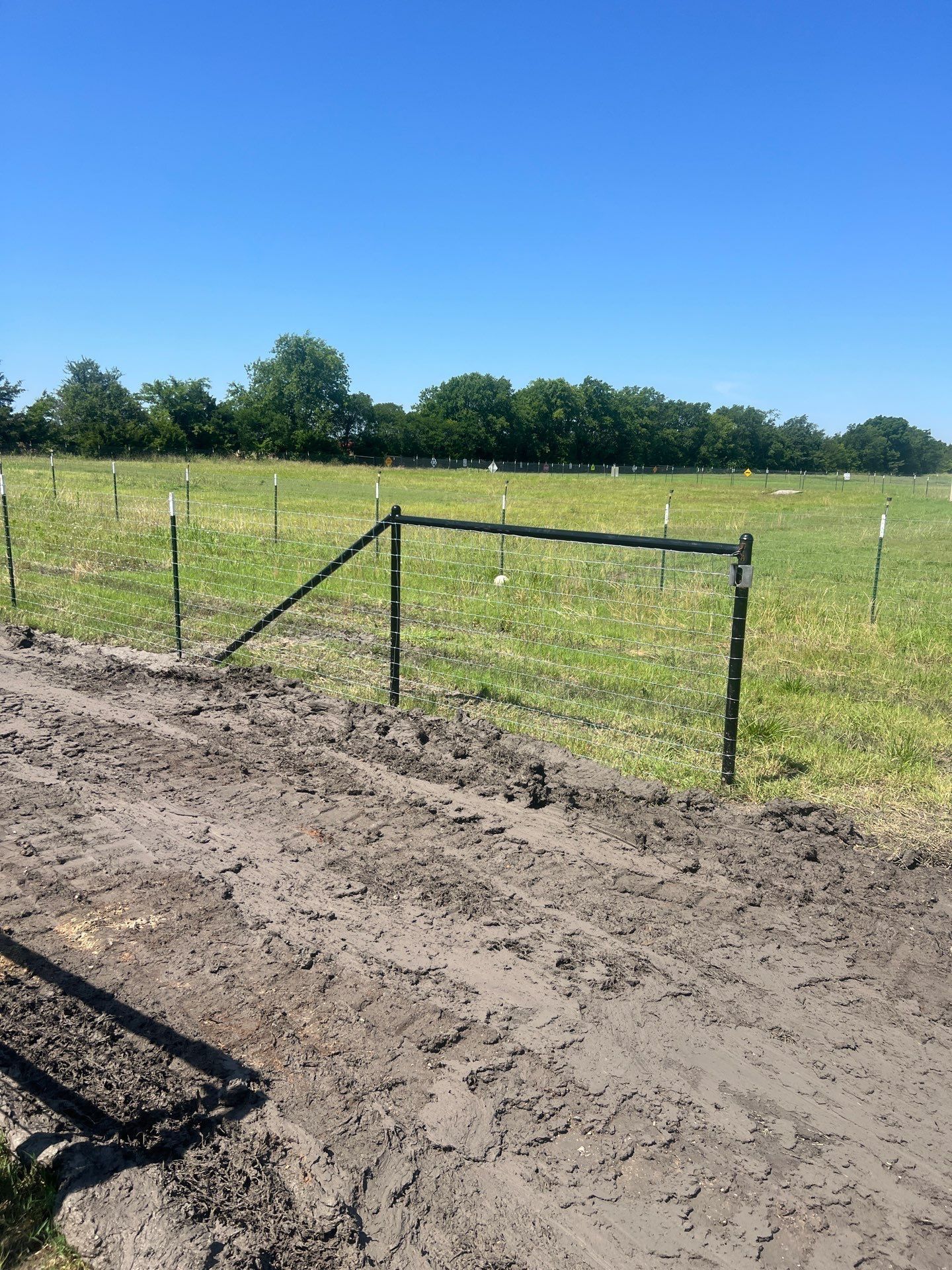 A dirt road going through a grassy field with a fence in the background.