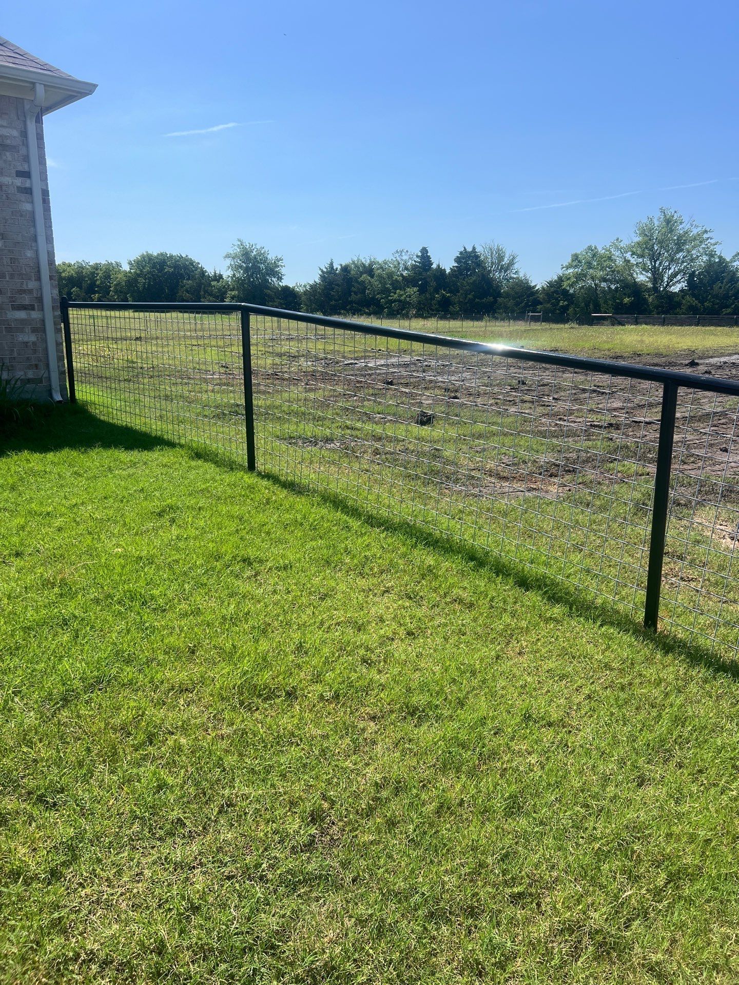 A fence surrounds a lush green field in front of a house.